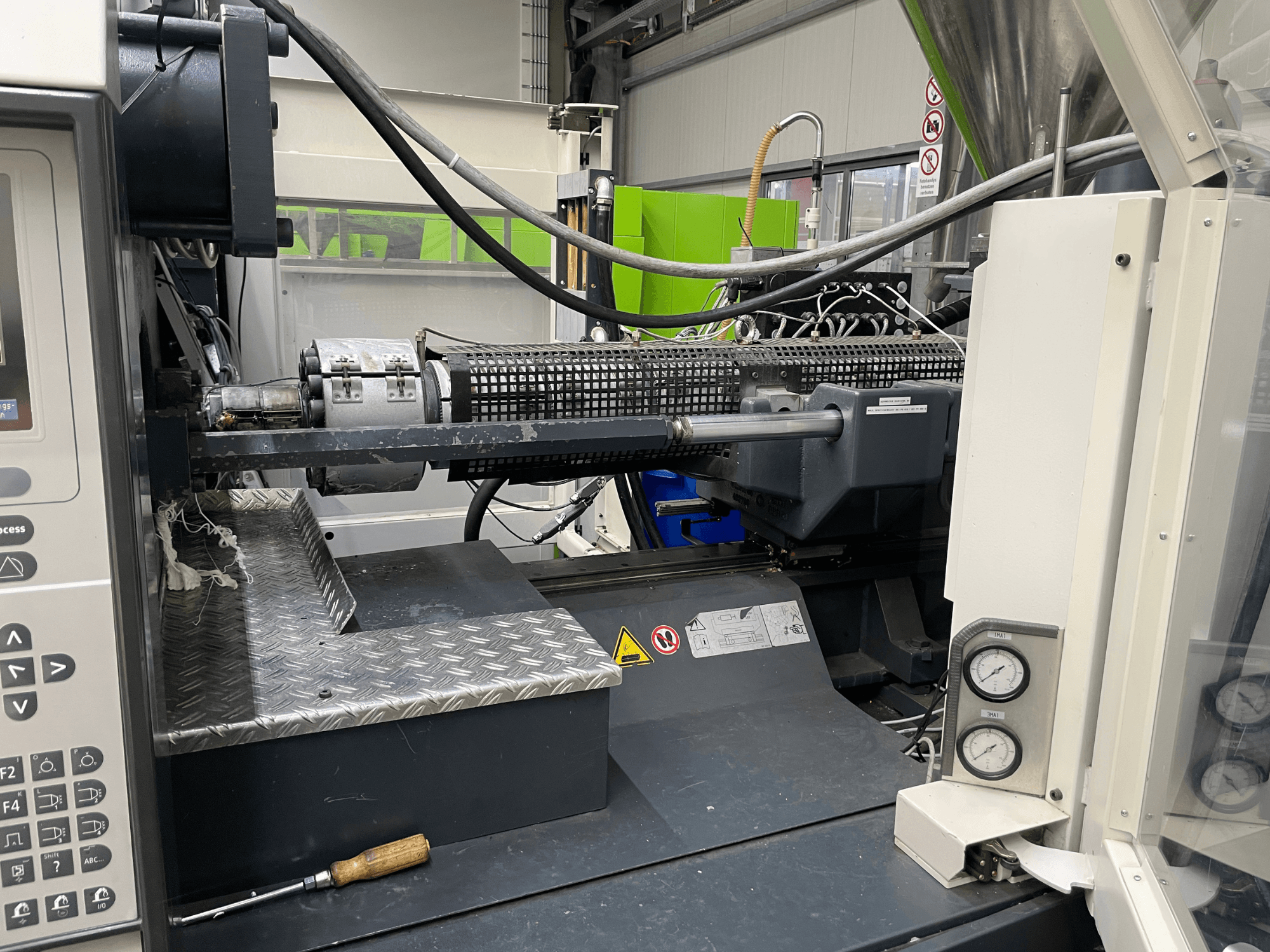 Ruiskuvalukoneen sivukuva, jossa ohjauspaneeli, ekstruuderi ja painemittarit näkyvät, ihanteellinen valmistustehtäviin.