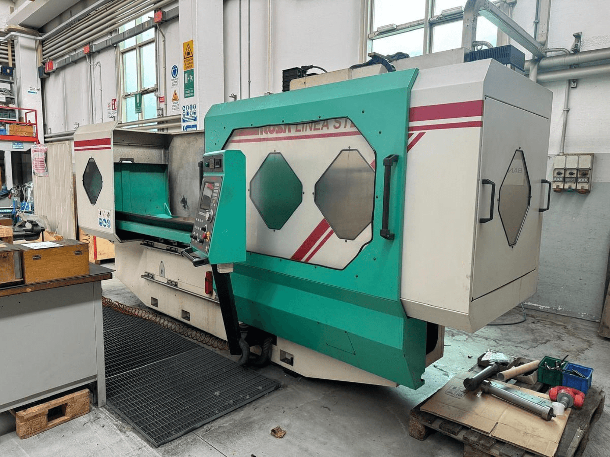 Vihreä ja valkoinen tarkkuuskone, etukuva, jossa ohjauspaneeli, työalue ja työkaluja kuormalavalla. Tuotemerkki: BAMB.