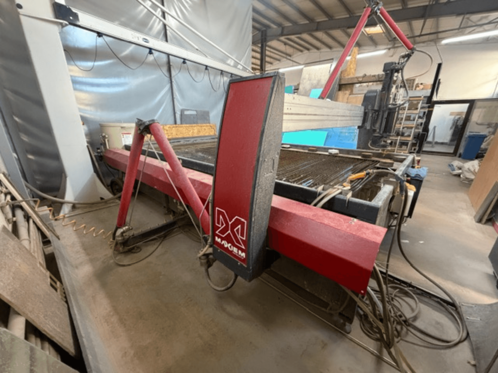 X-merkkinen punainen vesisuihkuleikkauskone sivulta katsottuna, jossa näkyy mekaaniset osat ja putkiston yksityiskohdat.