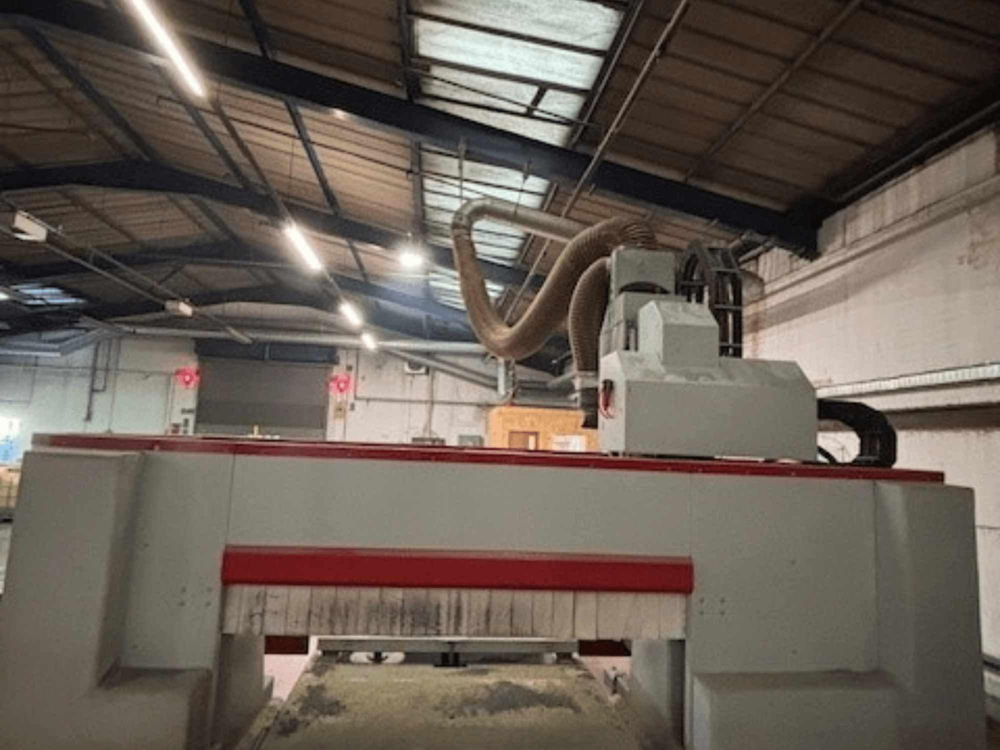 CNC-jyrsinkone työpajassa, sivukuva, jossa korostuu punainen ja harmaa muotoilu, pölynpoistojärjestelmä kiinnitetty.