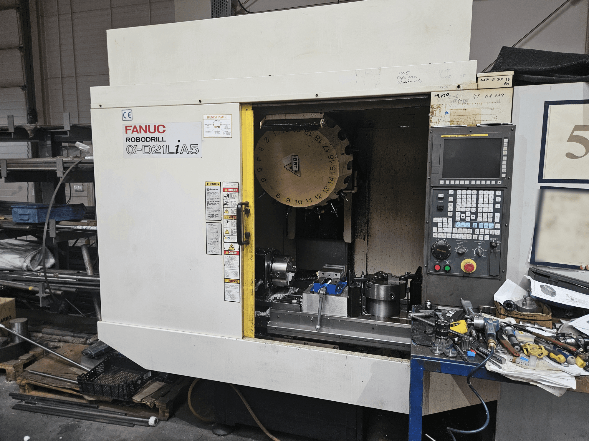 FANUC Robodrill α-D21LiA5, etukuva, jossa näkyy työkalunpidin ja ohjauspaneeli, työkalujen ja laitteiden ympäröimänä työpajassa.