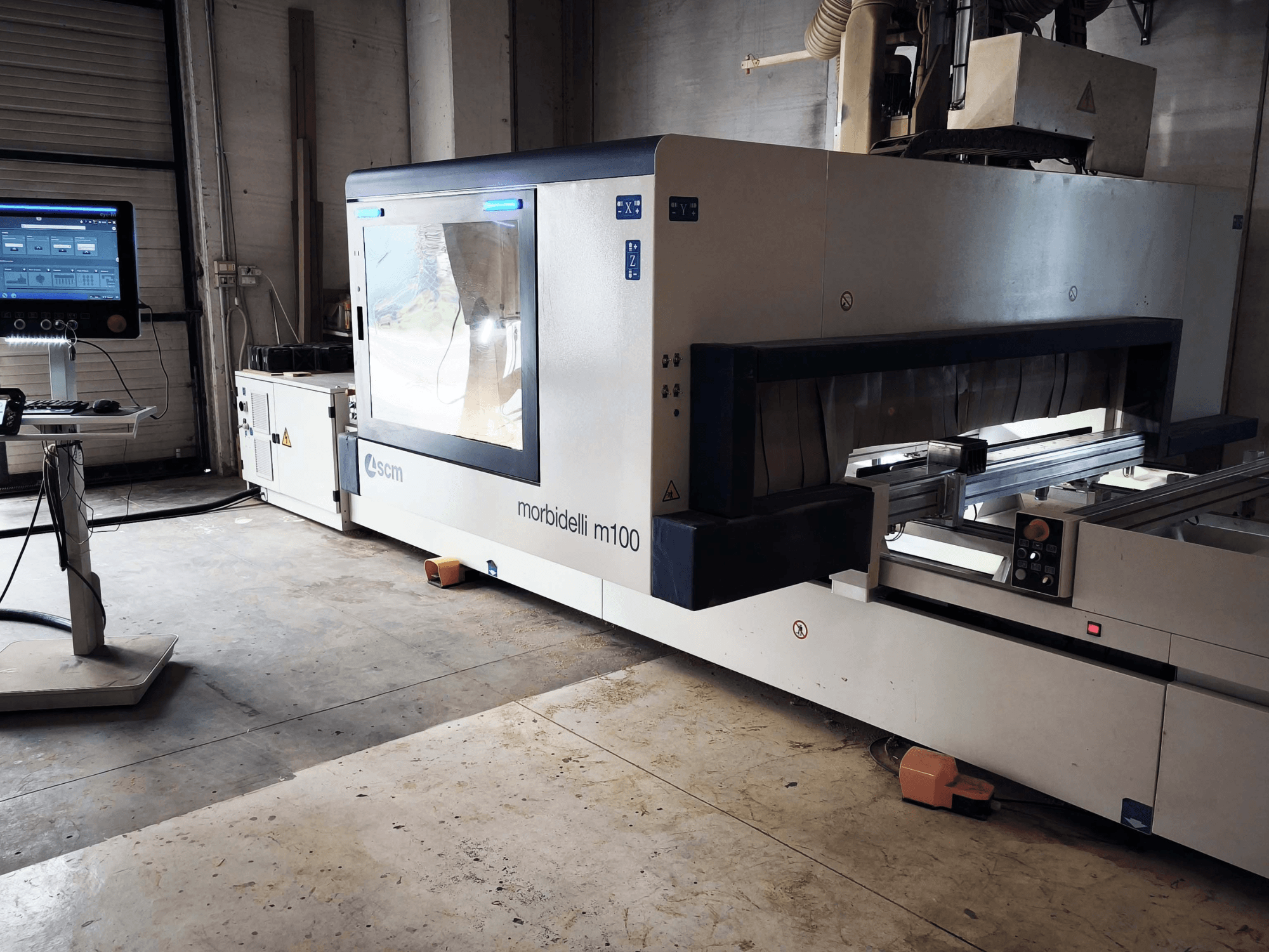 SCM Morbidelli M 100 CNC-puunkäsittelykeskus sivulta katsottuna; kuvassa näkyvät ohjauspaneeli, työtila ja turvallisuusominaisuudet.
