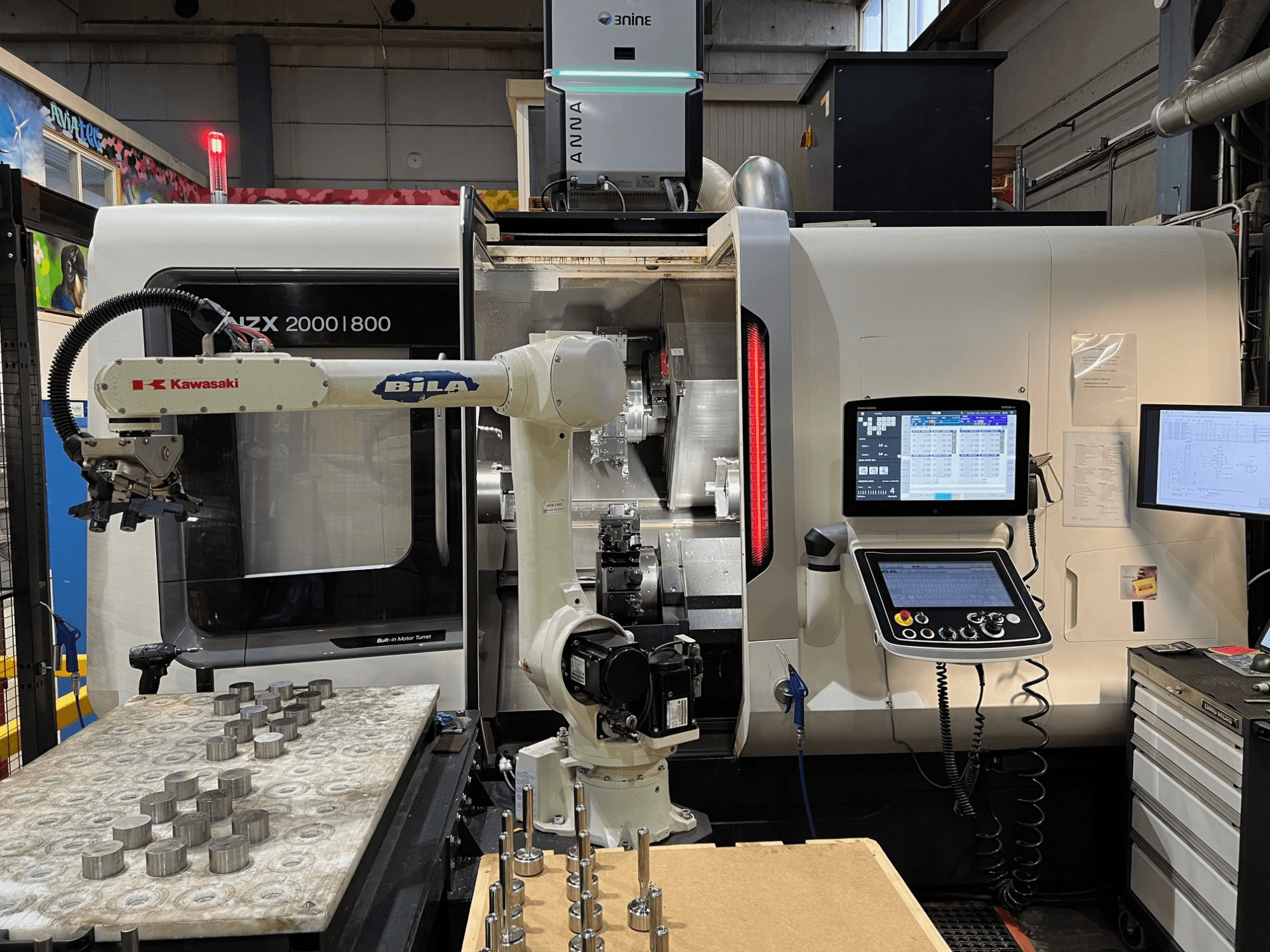 DMG MORI NZX 2000/800SY -vaakasuora sorvi työpajassa; kuvassa näkyvät Kawasakin robottivarsi ja ohjauslaitteet.