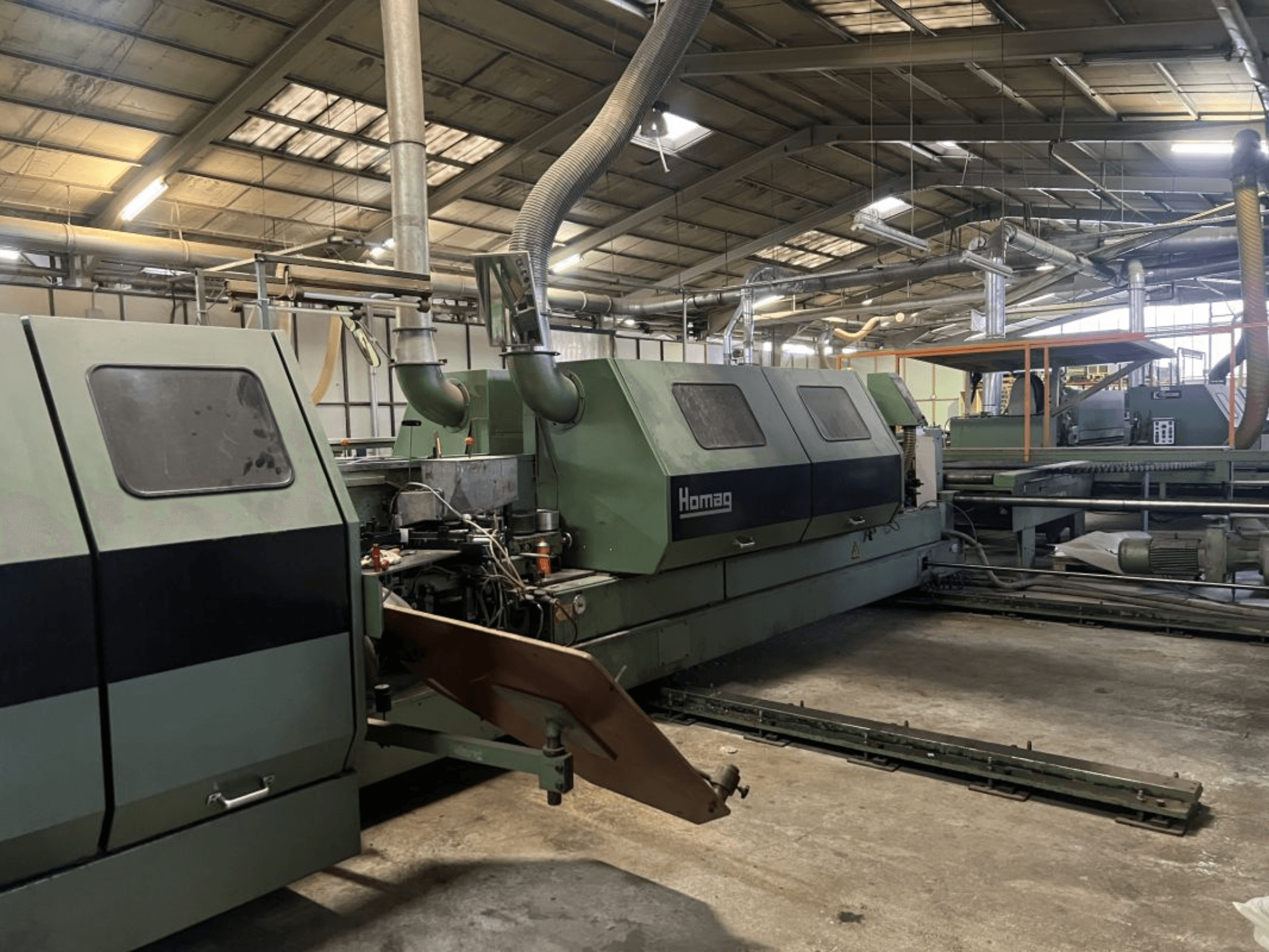 Vihreä Homag-teollisuuskone, sivukuva, jossa näkyy käyttöosia ja ohjauspaneeli varastossa.