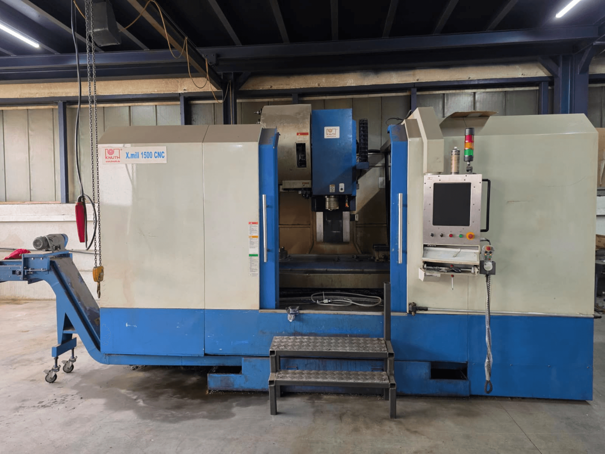 KNUTH X-MILL 1500 CNC-pystykoneistuskeskus, sivukuva, jossa näkyvät ohjauspaneeli, portaat ja poistokuljetin.