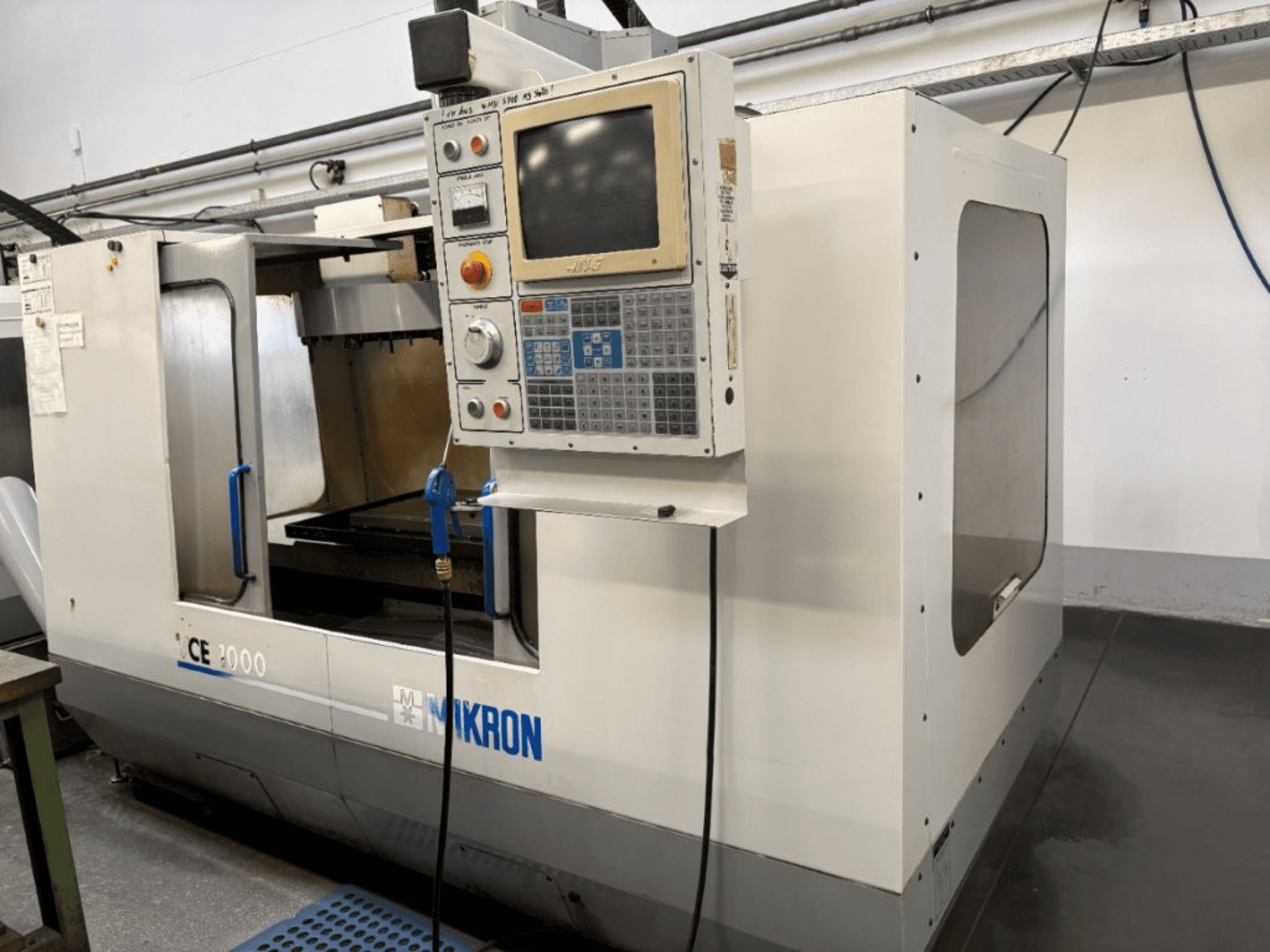 Mikron CE 2000 CNC-kone, etukuva; siinä on ohjauspaneeli, jossa on painikkeet ja näyttö, hopeinen ulkokuori ja työskentelyalue.