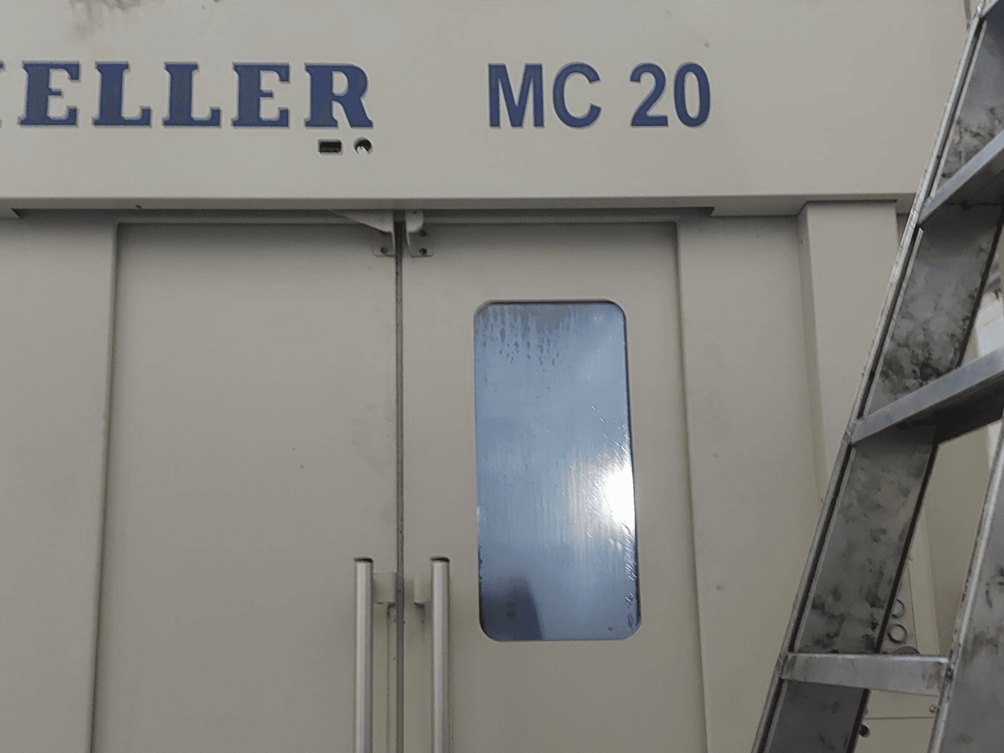 HELLER MC 20 -vaakakäsittelykeskuksen etukuva, jossa näkyy ovenkahvat ja pieni ikkuna. Tikkaat sivulla.