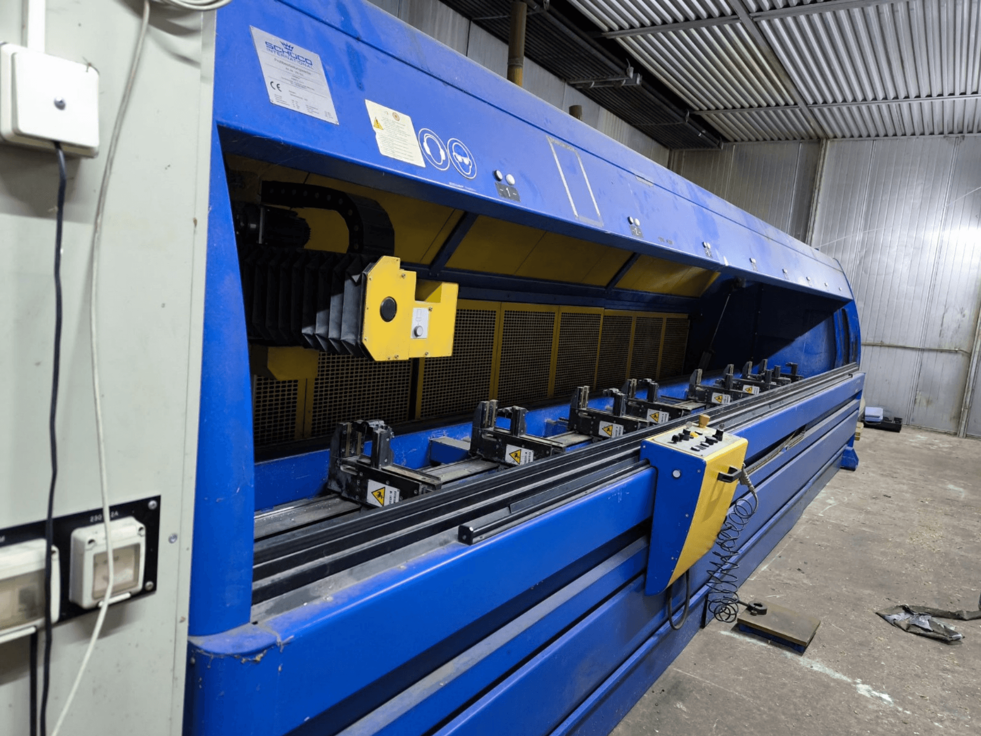 Sininen Schneider-teollisuusleikkauskone, sivukuva, jossa ohjauspaneeli, hihnat ja useita kiinnitysasemia näkyvissä.