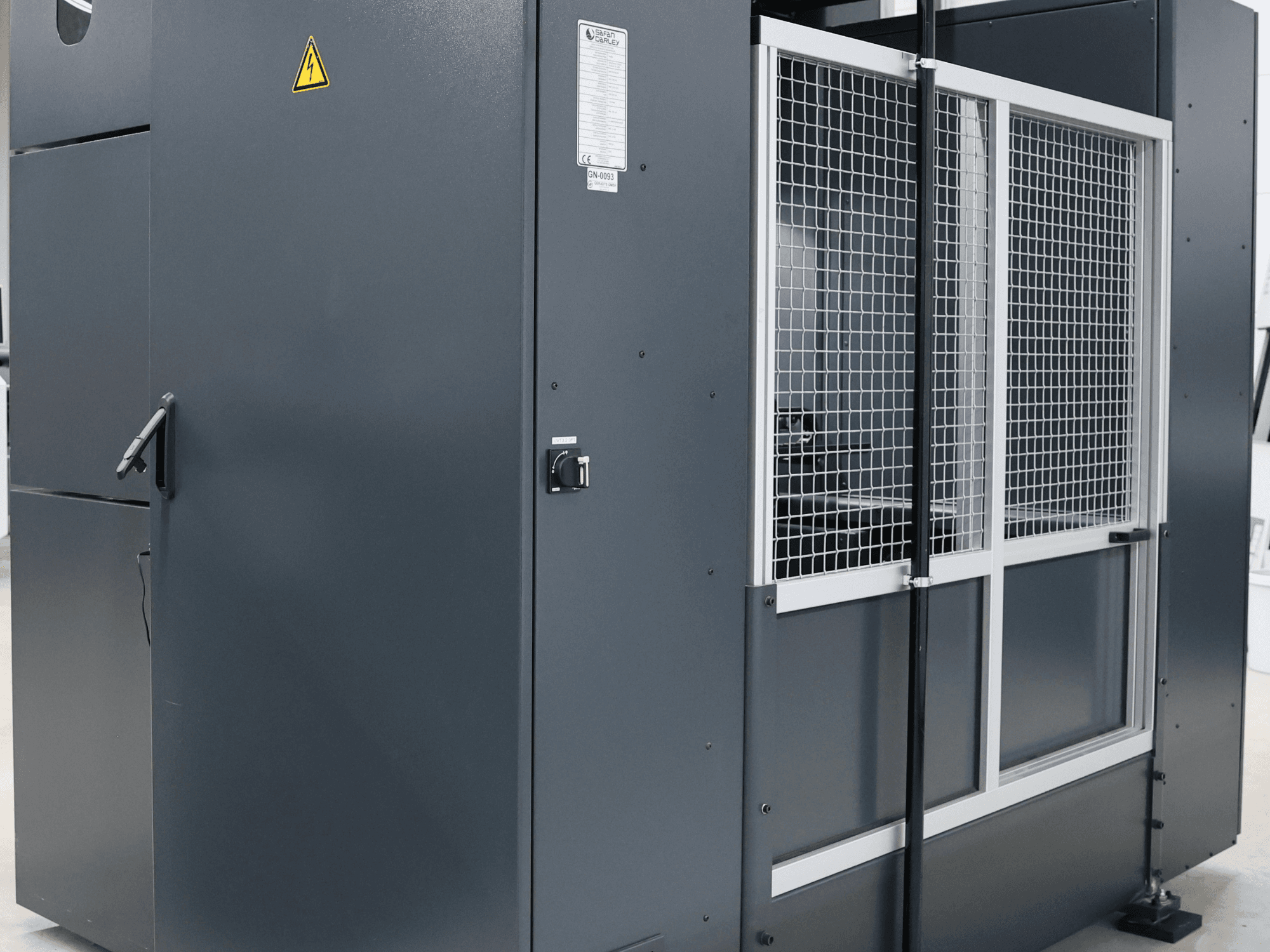 Harmaa teollisuuskone, jossa on turvavaroitus, etukuva, jossa näkyy verkko-ovi ja ohjauspaneeli, malli merkitty.
