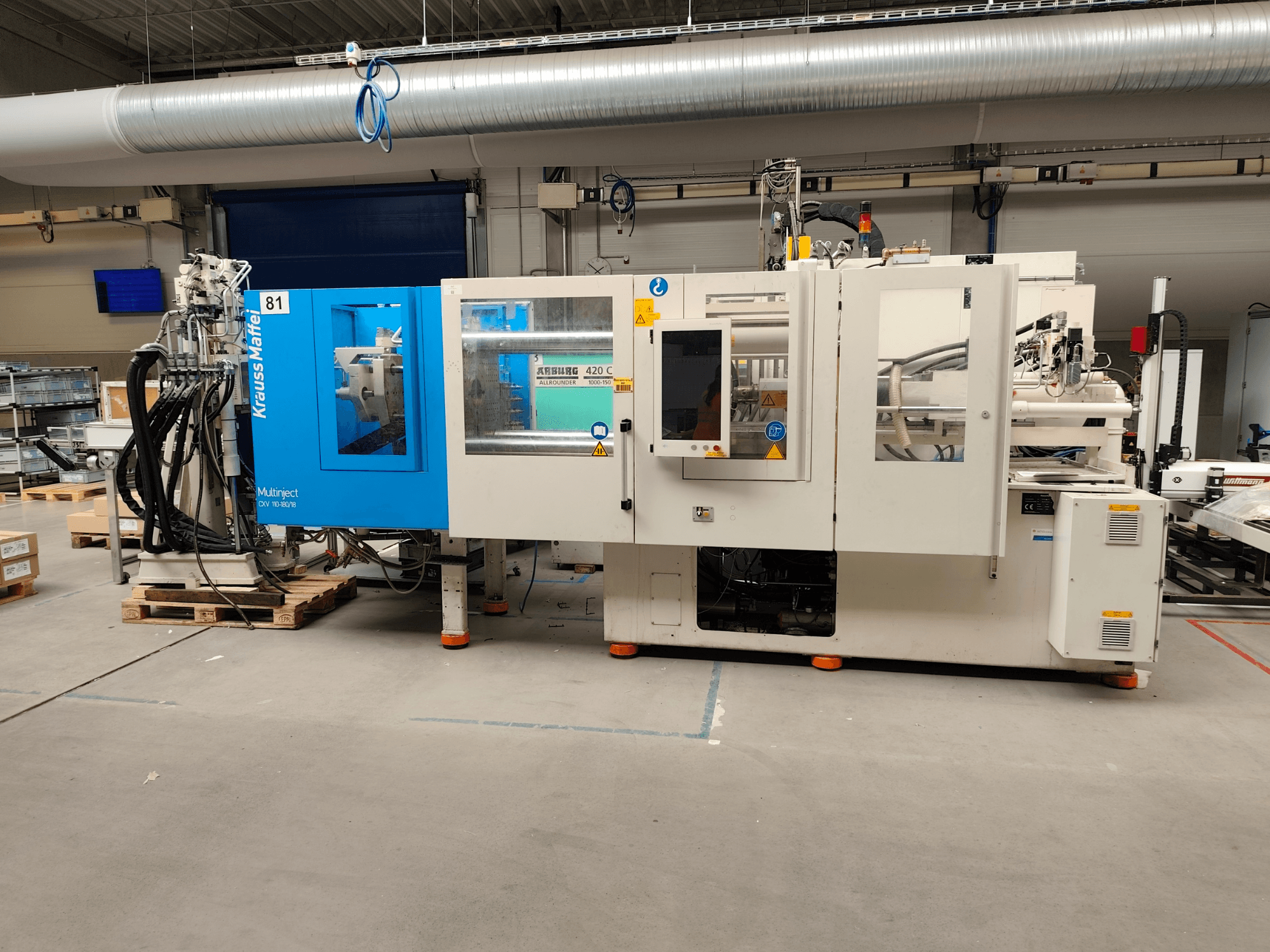 Krauss Maffei 110-180-180 CX V -hydraulinen ruiskupuristuskone, sivukuva, jossa näkyy sinivalkoinen runko, ohjauspaneeli ja liittimet.