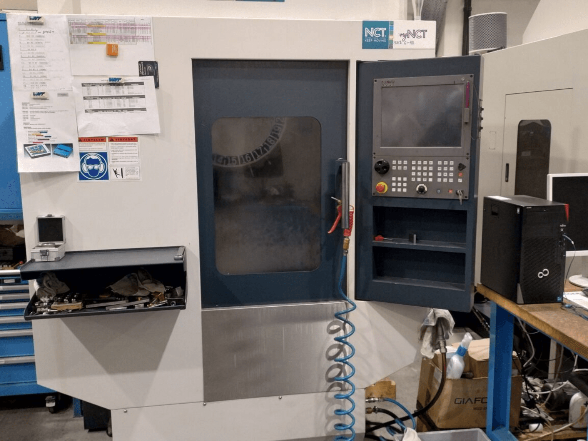 NCT CNC-kone, etukuva, jossa on ohjauspaneeli, jossa on numeronäppäimistö, työkalut säilytyslaatikossa ja käyttöohje seinällä.