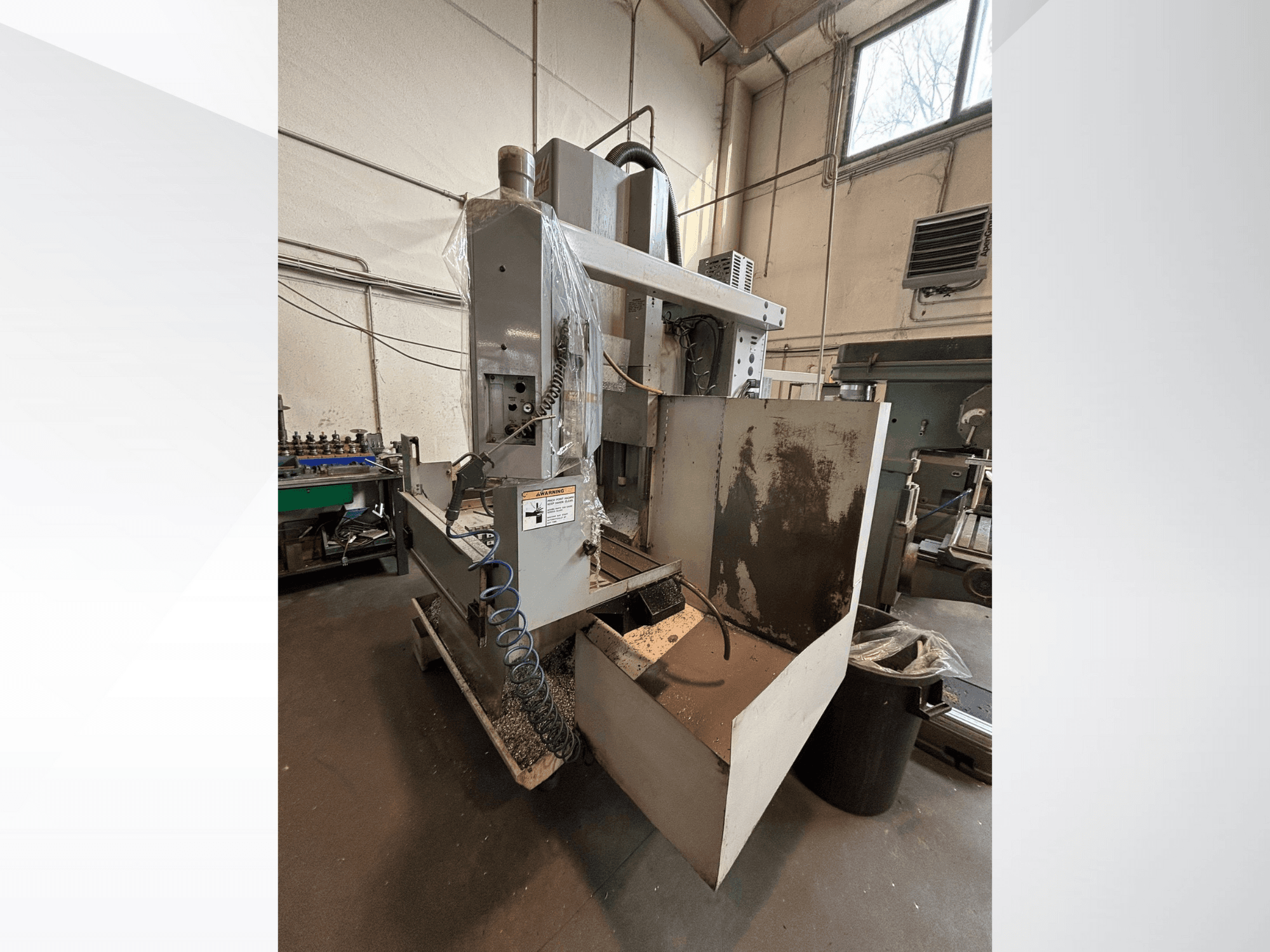 Pystyjyrsinkone suojapeitteellä, sivukuva; jäähdytysnesteletku ja ohjauspaneeli näkyvissä. Ihanteellinen koneistukseen.