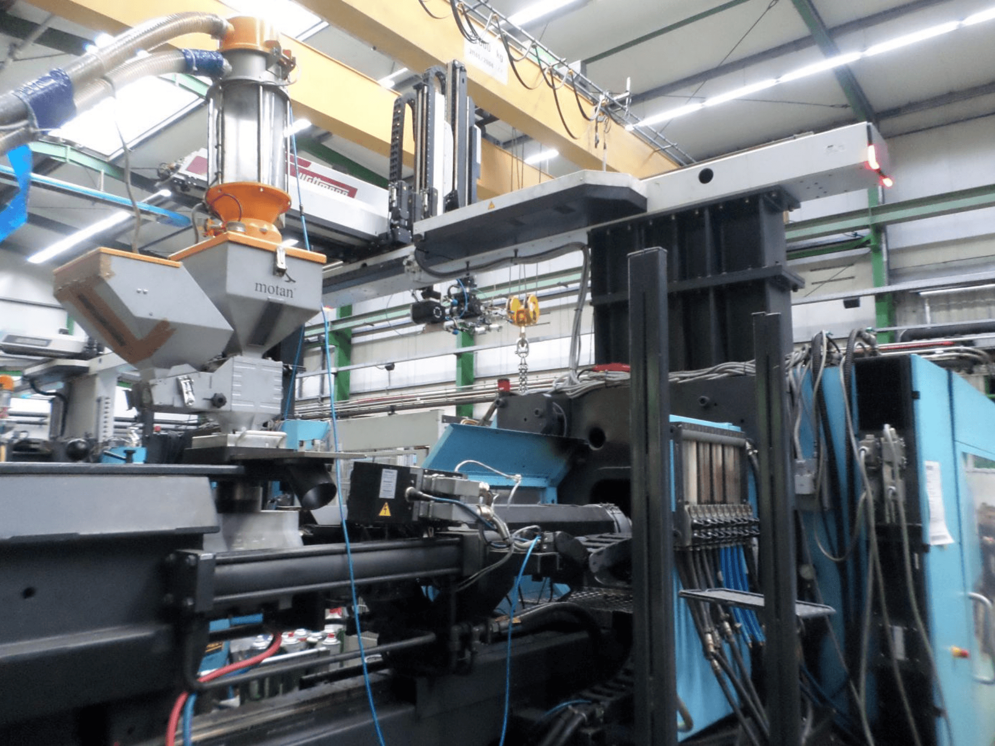 Hydraulinen ruiskuvalukone DEMAG D 1300, sivukuva, jossa näkyvät syöttösuppilo, ohjausyksikkö ja liitännät tehdasasetuksissa.