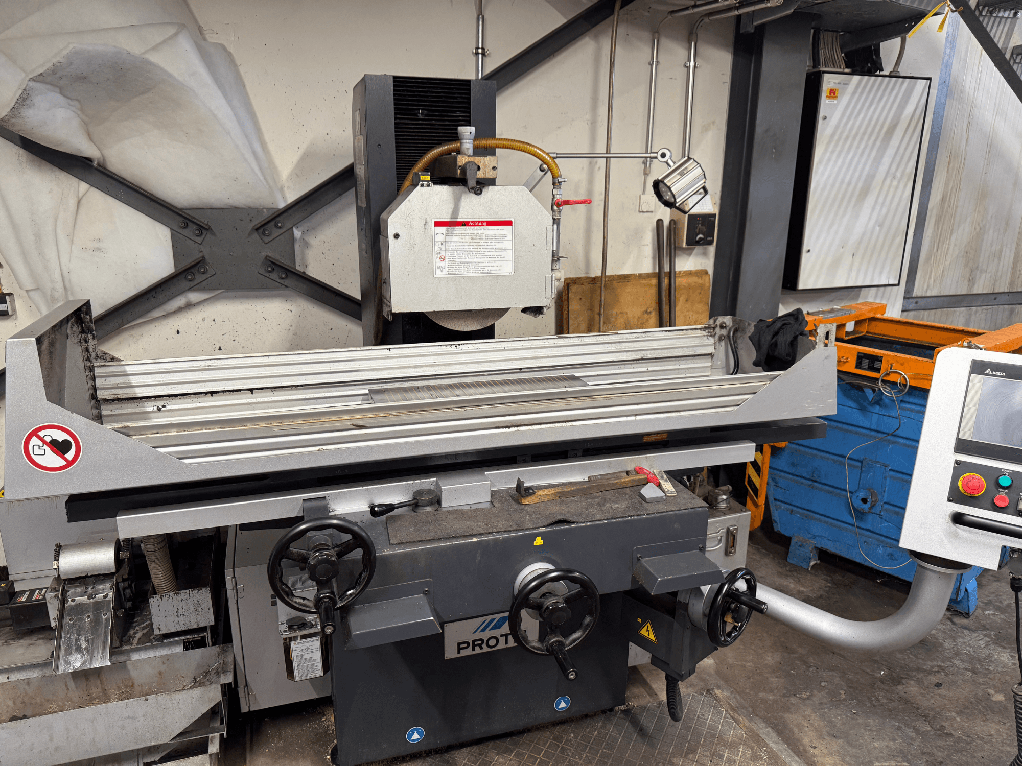 PROTEC-kone, etukuva, jossa näkyy pintahiomakone, jossa on käsisäätimet, turvavaroitukset ja jäähdytysjärjestelmä.