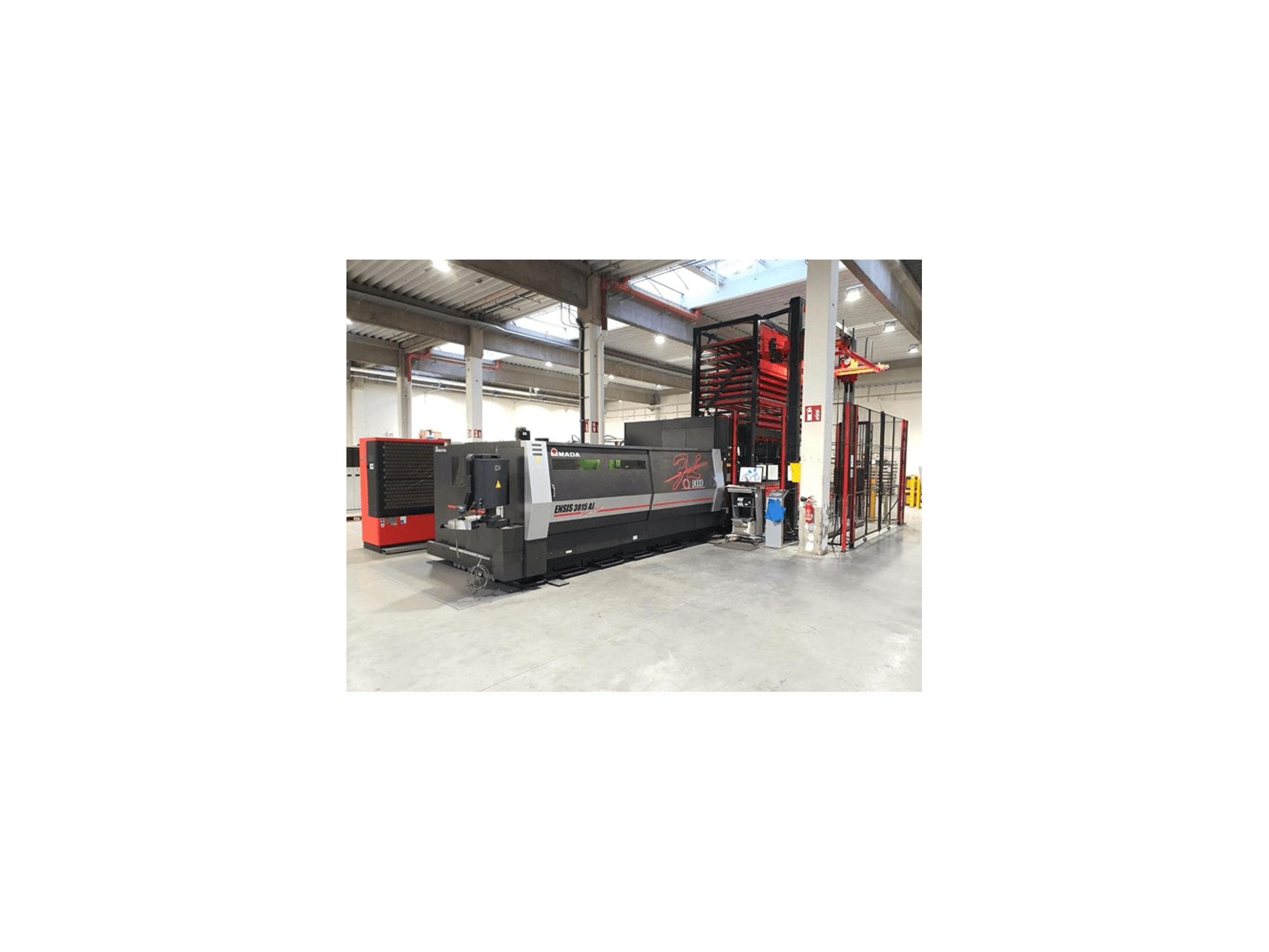 Amada ENSIS 3015 Aj -laserleikkauskone edestäpäin tilavassa teollisuusverstaassa, jossa on metallihyllyt.