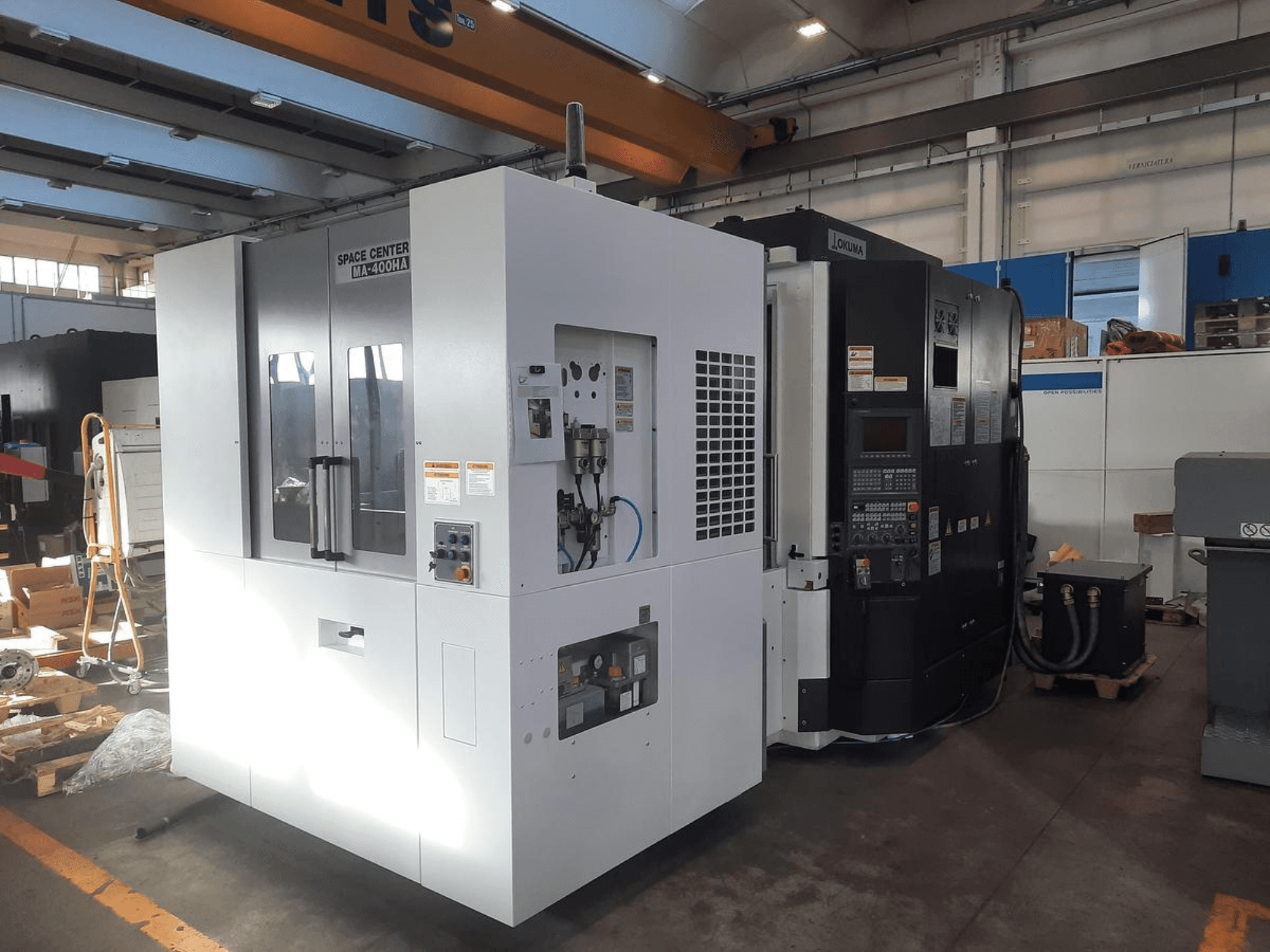 SPACE CENTER IM-400HAA- ja OKUMA CNC-koneiden etukuva, jossa näkyvät erilaiset hallintalaitteet ja valmistajan tarrat.
