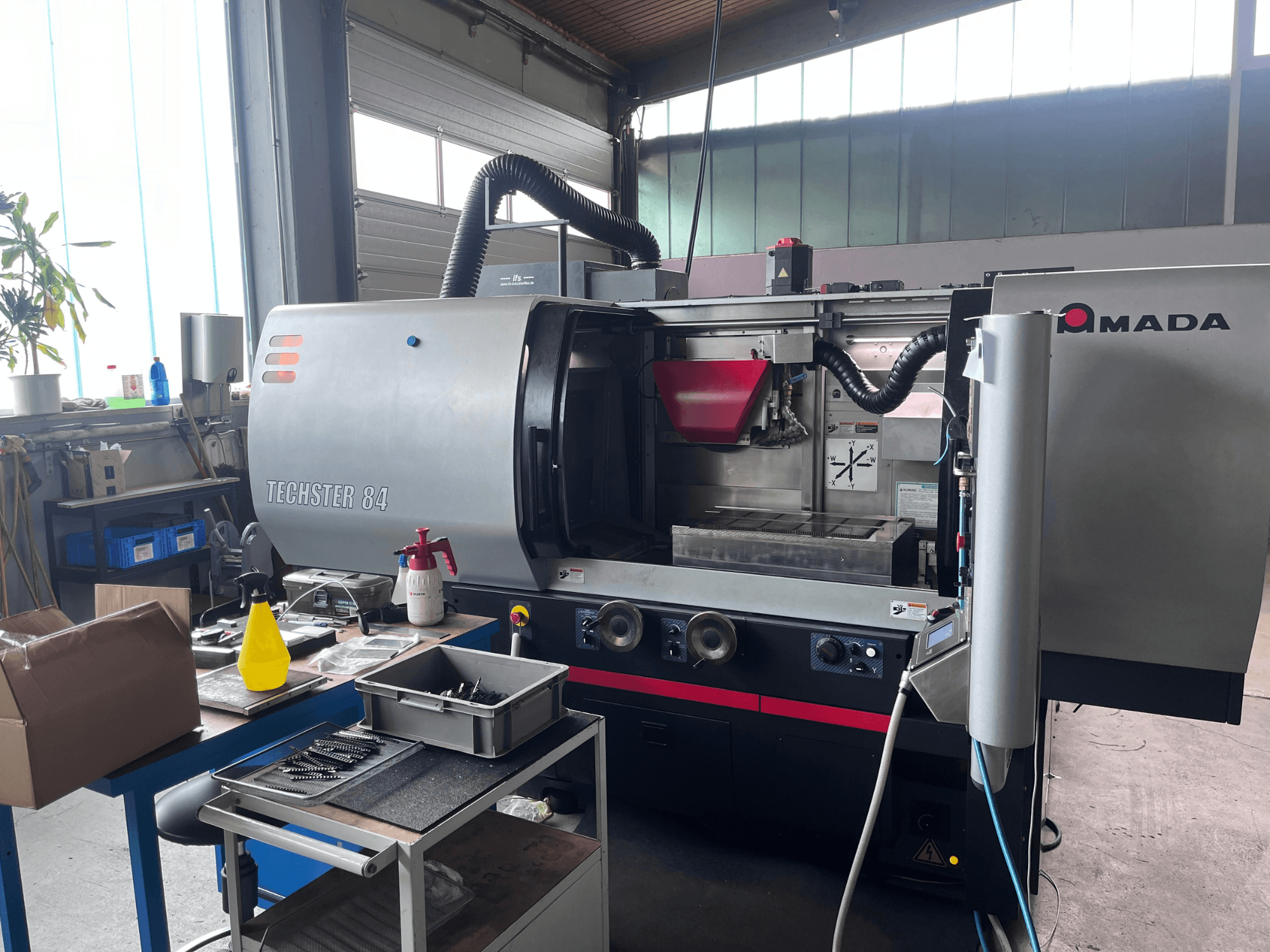 AMADA Techster 84 -pintahiomakone työpajassa; kuvassa etunäkymä, jossa näkyvät käyttölaitteet ja punainen syöttösuppilo.