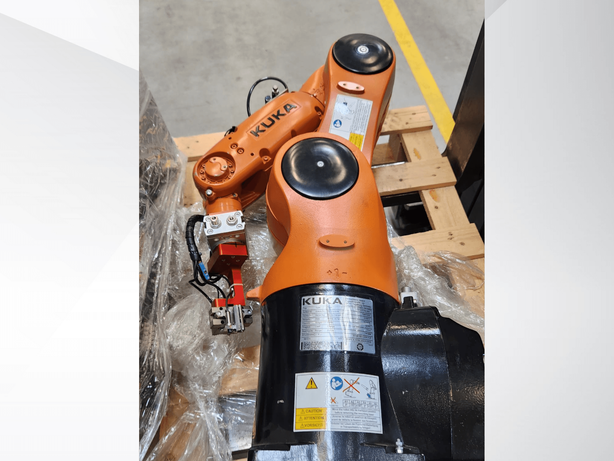 KUKA-robottivarsi oranssilla maalilla, sivukuva, jossa on tarttuja ja ohjausjohdot puisella kuormalavalla.