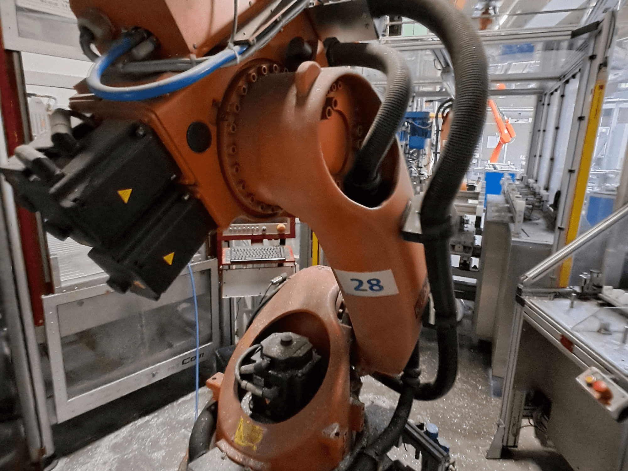 Lähikuva KUKA KR30-3 -robottivarresta, jossa on oranssi runko ja numero 28, sekä moottorit ja johdot sivulta katsottuna.