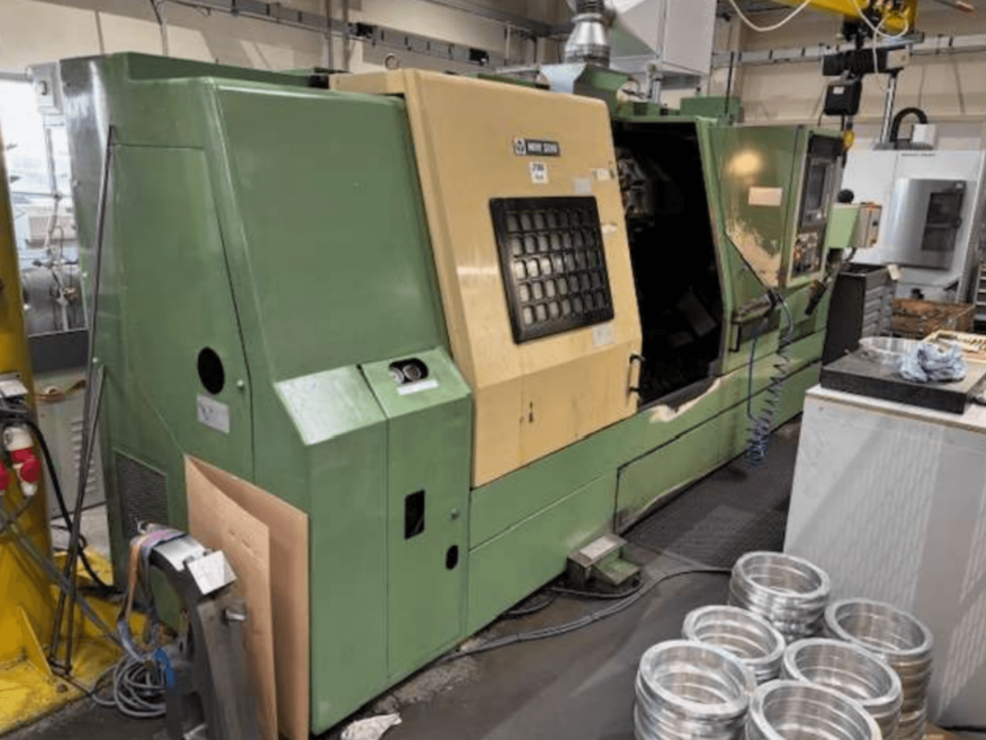 Mazakin vihreä CNC-sorvi edestä katsottuna, jossa on ohjauspaneeli ja työstettyjä alumiiniosia työpöydällä.