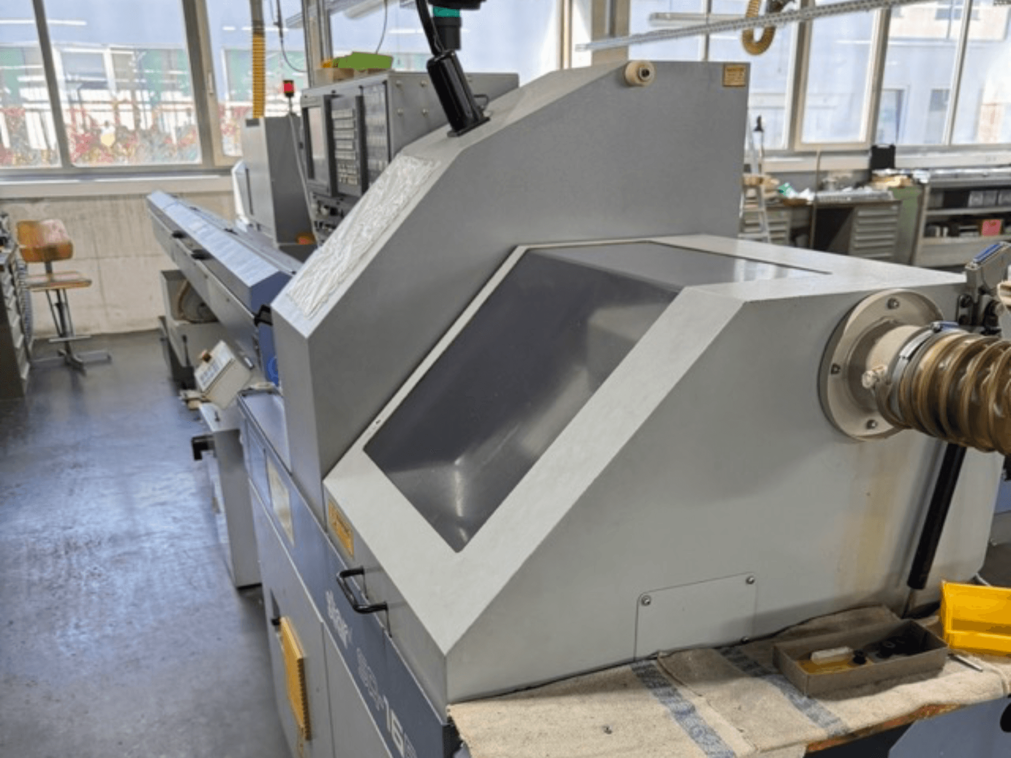 Harmaassa teollisuuskoneessa on sivulta katsottuna suuri kulmikas paneeli, ohjauspainikkeet ja letkukiinnitys.