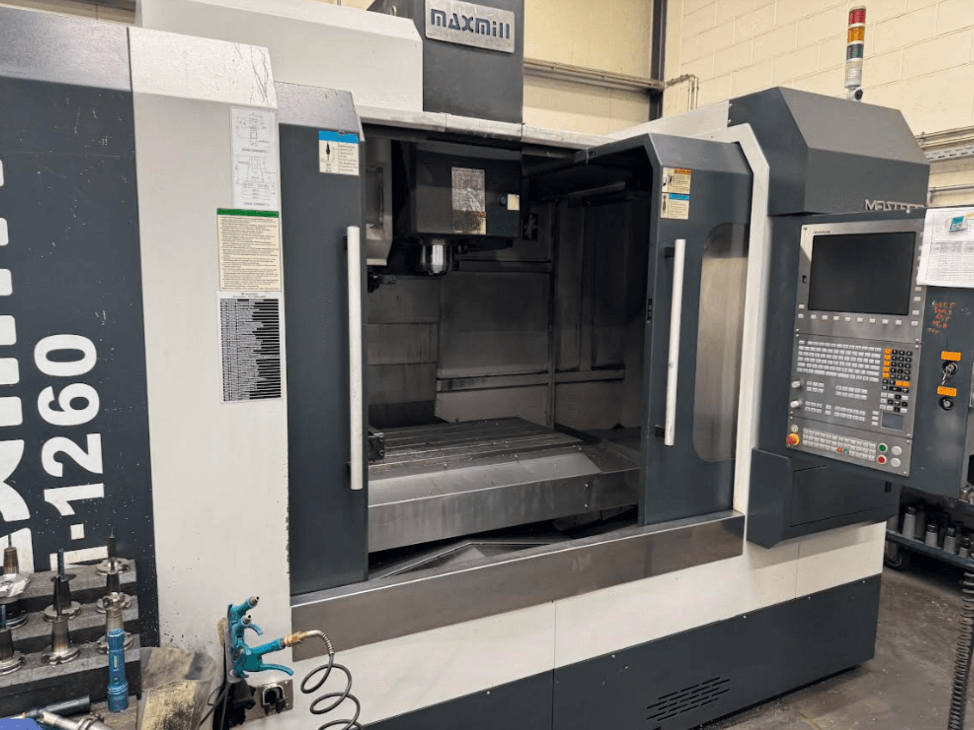 Maxmill CNC-jyrsinkone, malli M-1260, etukuva, jossa tyhjä työtila, ohjauspaneeli ja käyttöohjeet.