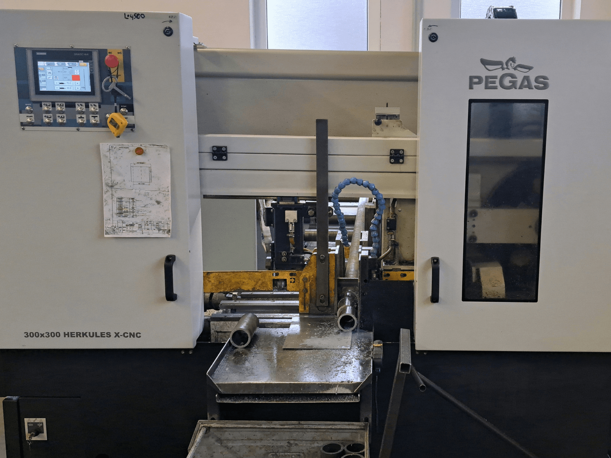 Pegas HERKULES X-CNC 300x300 -metallileikkauskone, etunäkymä, jossa näkyy ohjauspaneeli ja työalue metallikappaleineen.