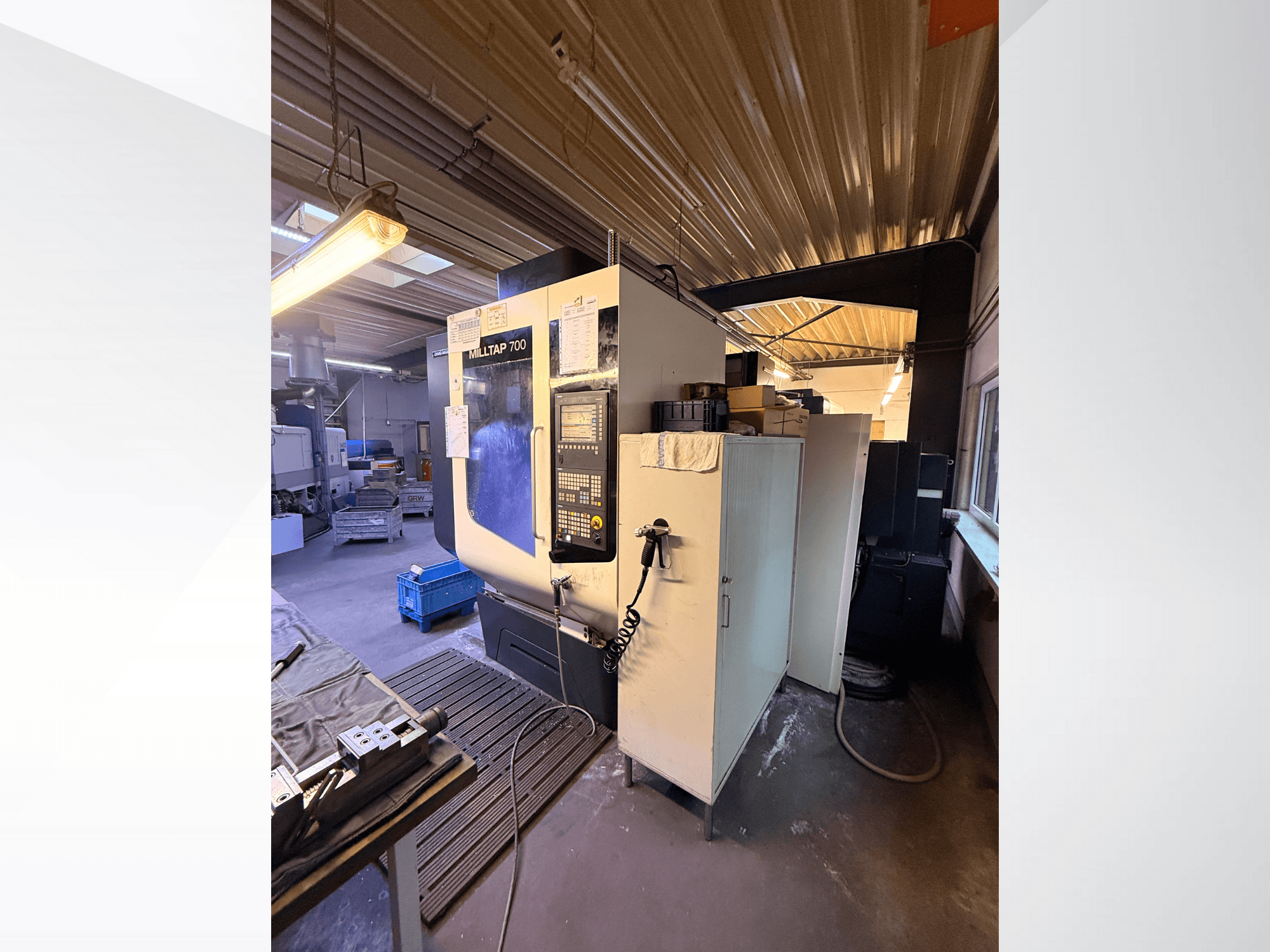 Milltap 700 CNC-kone työpajassa; etunäkymässä näkyy ohjauspaneeli, työkaluhyllyt ja varastotilat, joiden yläpuolella on valaistus.