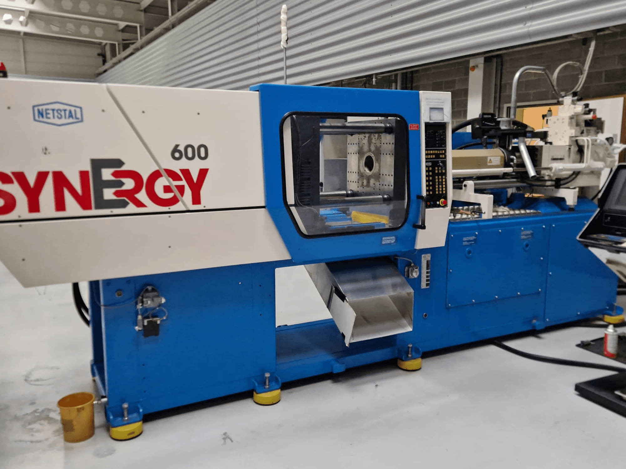 Netstal Synergy 600-230 hydraulinen ruiskuvalukone, sivukuva, jossa näkyy ohjauspaneeli ja ruiskutusalue.