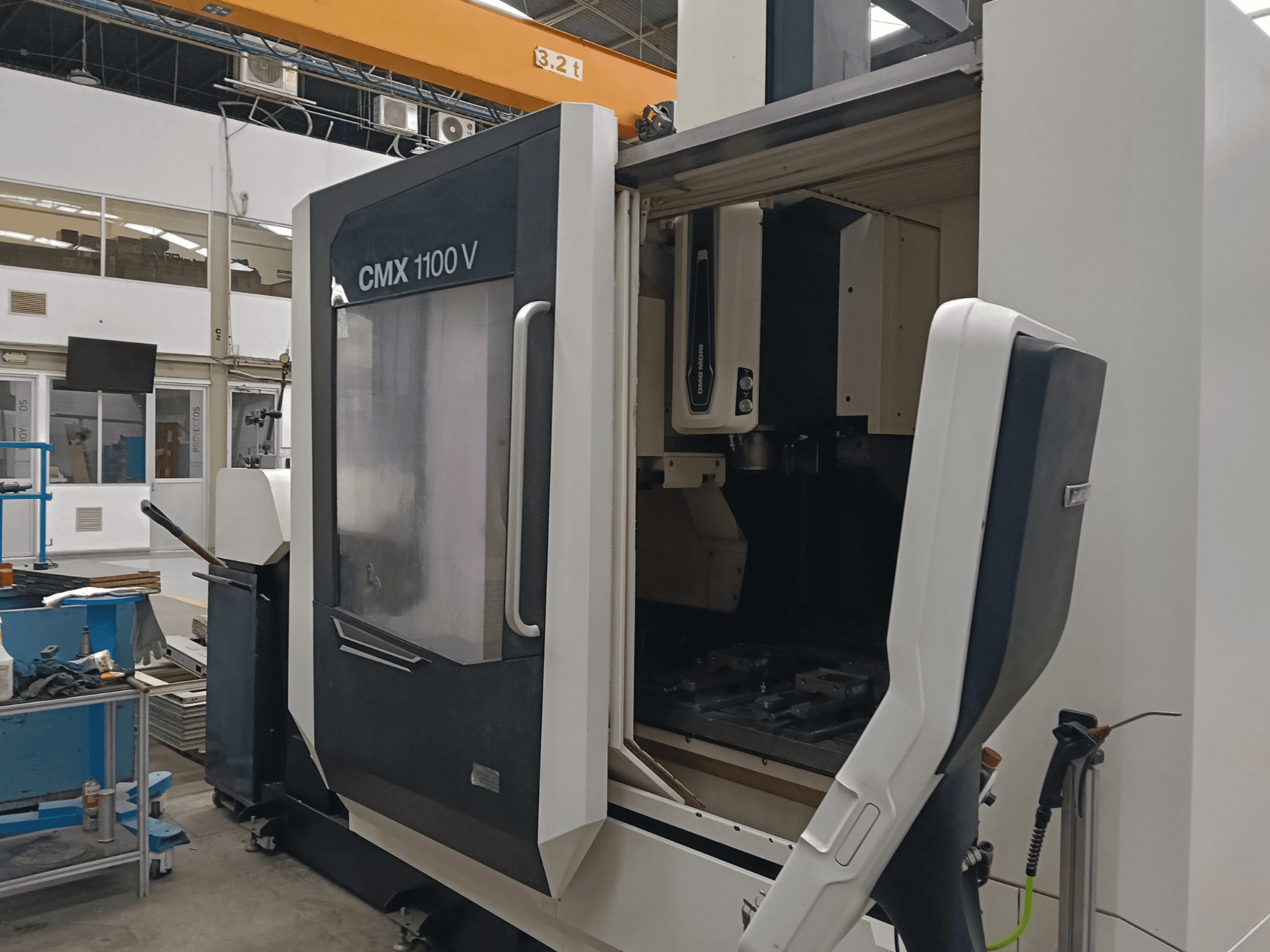 DMG MORI CMX 1100 V -pystykoneistuskeskus, etunäkymä, jossa näkyy avoin luukku ja koneen sisällä oleva työkalujärjestely teollisuustiloissa.