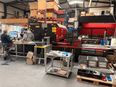 AMADA LC-2415αIII CO2-laserleikkauskone työpajaympäristössä, etualalla näkyy tietokonepiste.