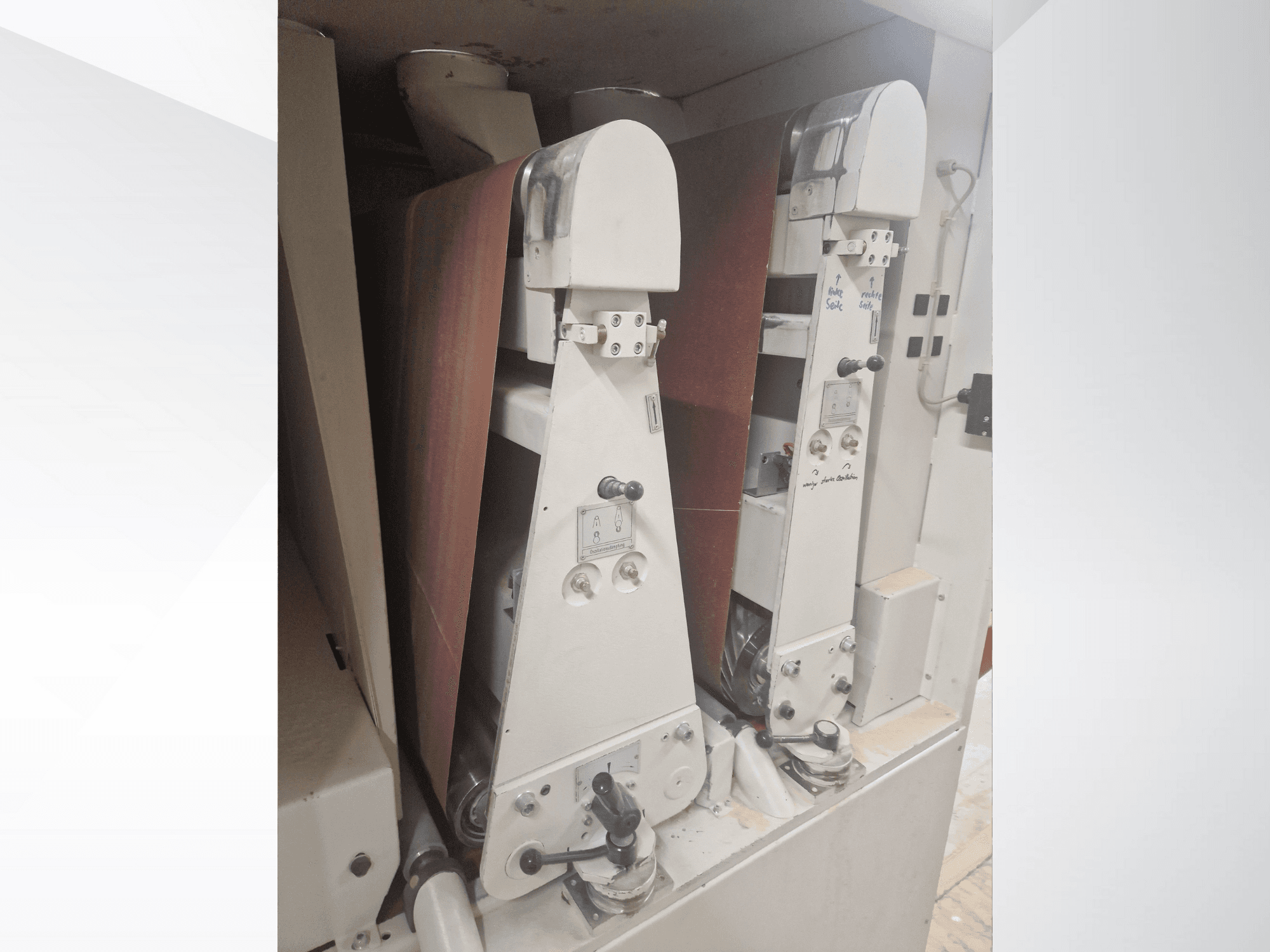 Kaksi teollisuushiontakonetta, joissa on punaiset hiomanauhat, etukuva, jossa näkyvät hallintalaitteet ja metalliosat.