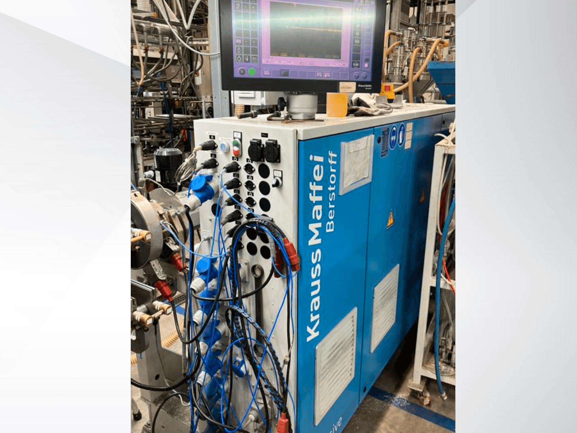 Krauss Maffei Berstorff -teollisuuskone, jossa on ohjauspaneeli ja näyttö, jossa on erilaisia painikkeita ja liitettyjä letkuja, sivukuva.