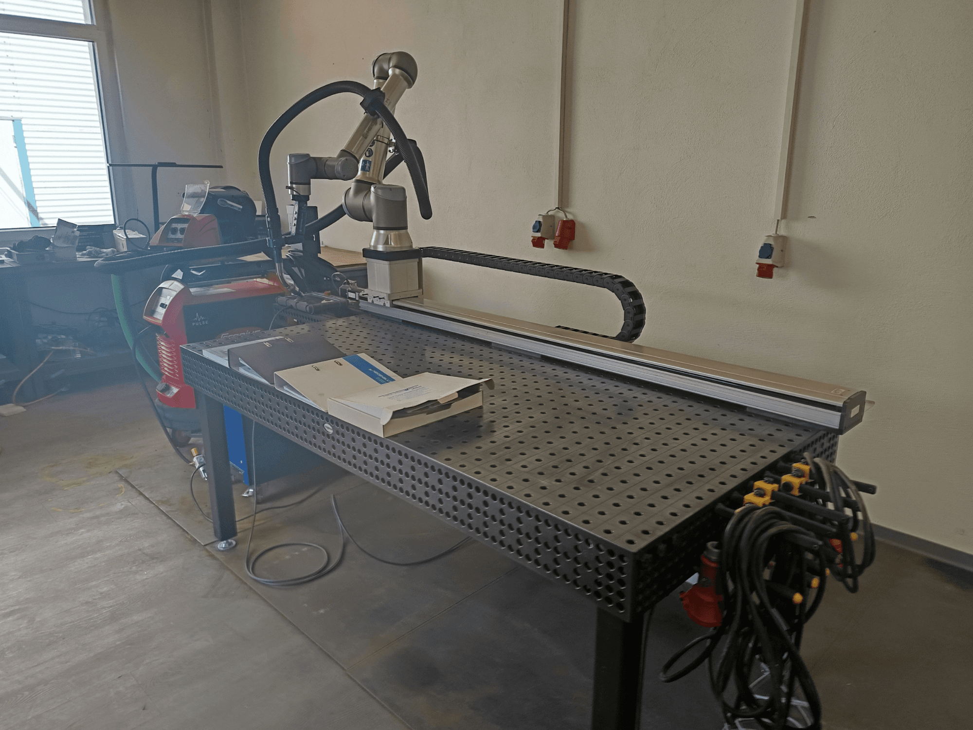 FRONIUS TransSteel 4000 -pulssihitsausyksikkö sivulta katsottuna; kuvassa näkyvät robottivarsi, työtila ja virtaliitännät.