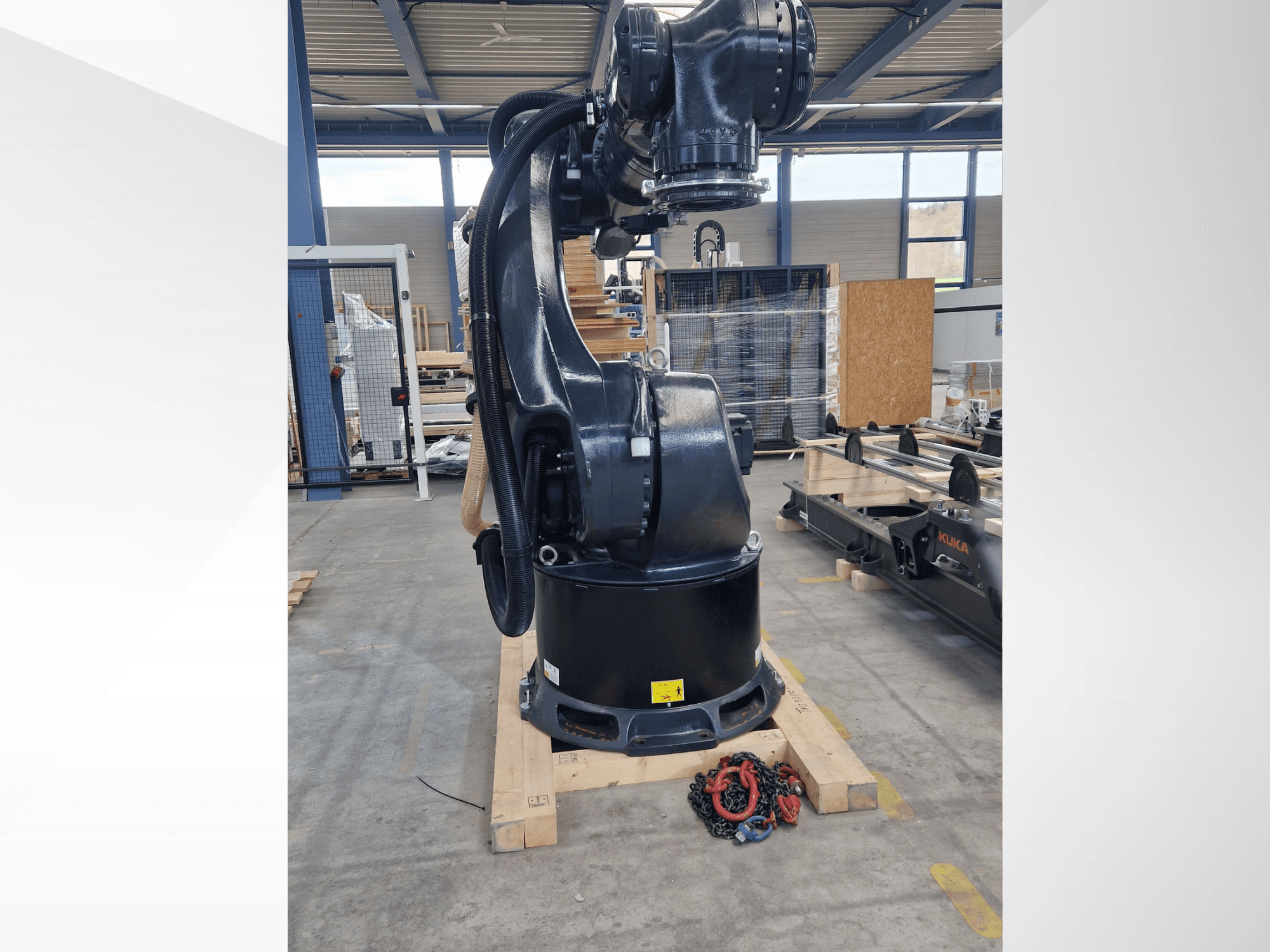 KUKA KR 340 R3330 -robottivarsi varastossa; sivukuva, jossa näkyvät sen jalusta ja kaapelit, etualalla ketjut.