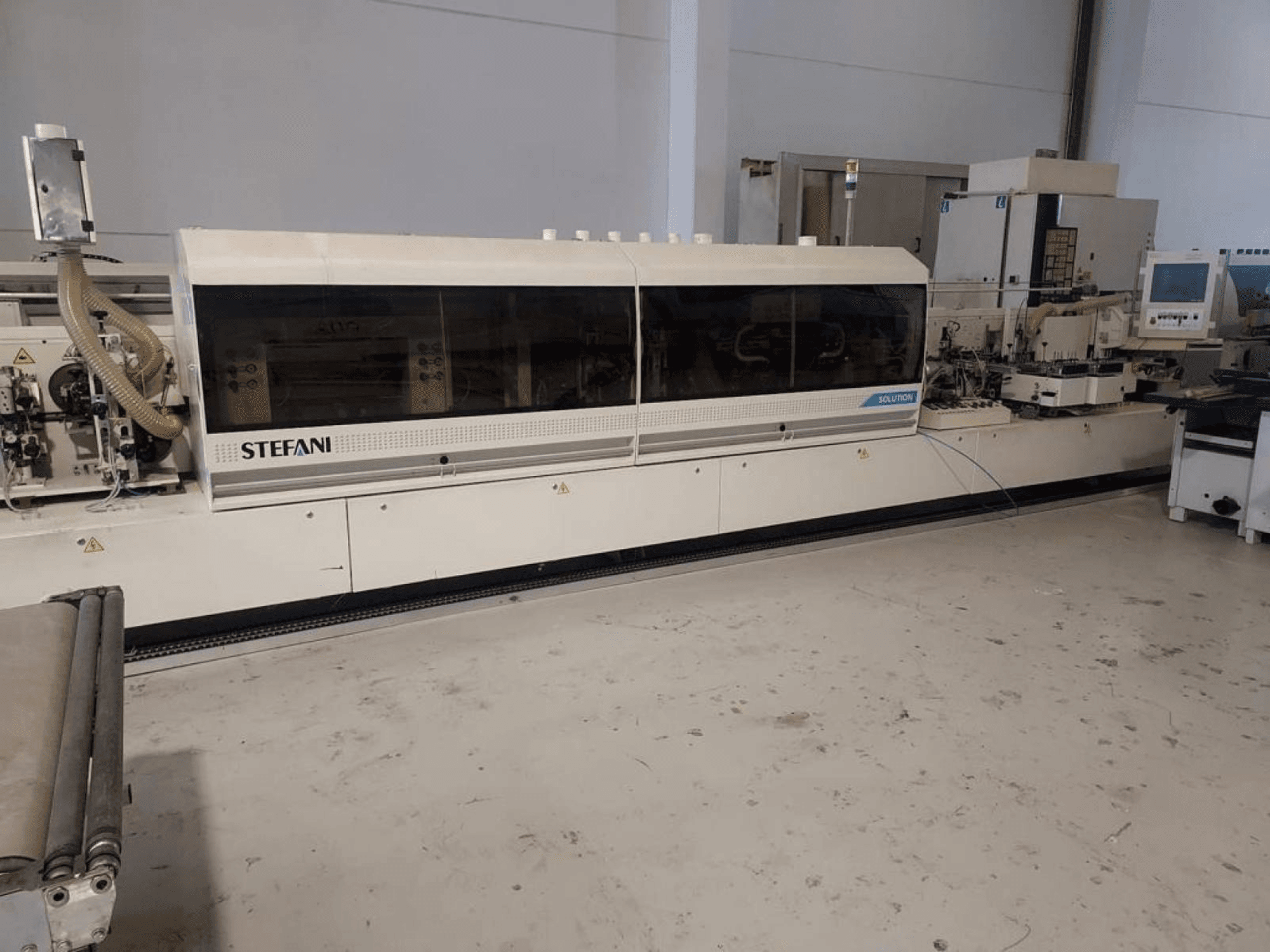 Stefani Solutions -reunanauhakone, etukuva, pölynpoistojärjestelmä ja ohjauspaneeli näkyvissä, työpajassa.
