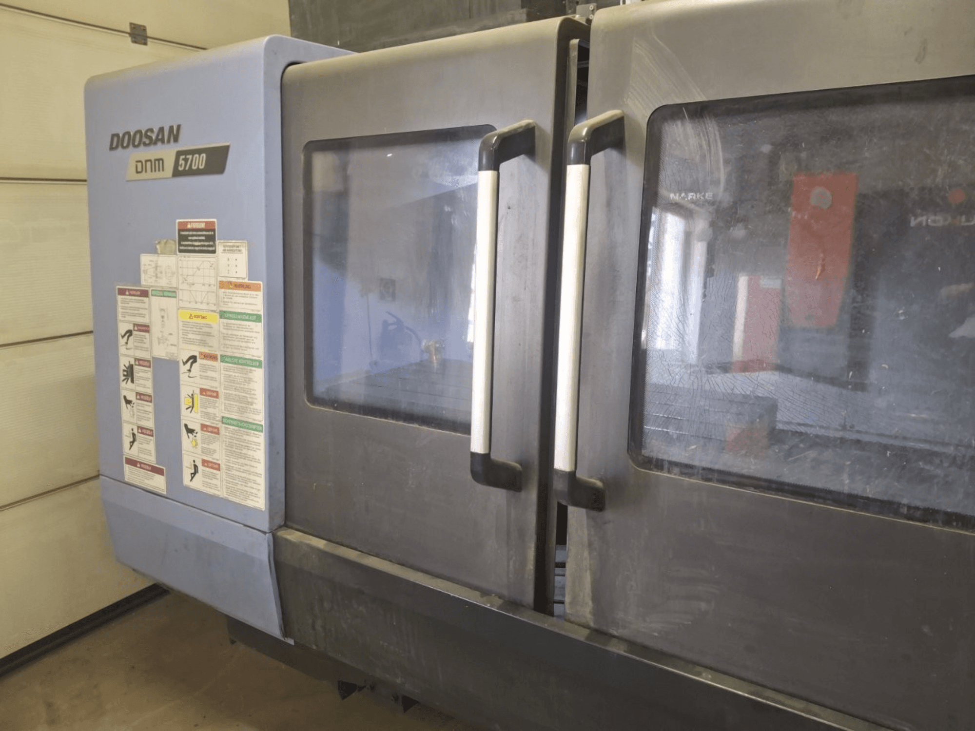 DOOSAN DNM 5700 -pystykäsittelykeskuksen etukuva, jossa on kaksoisovet ja käyttöohjeilla varustetut ohjauspaneelit.