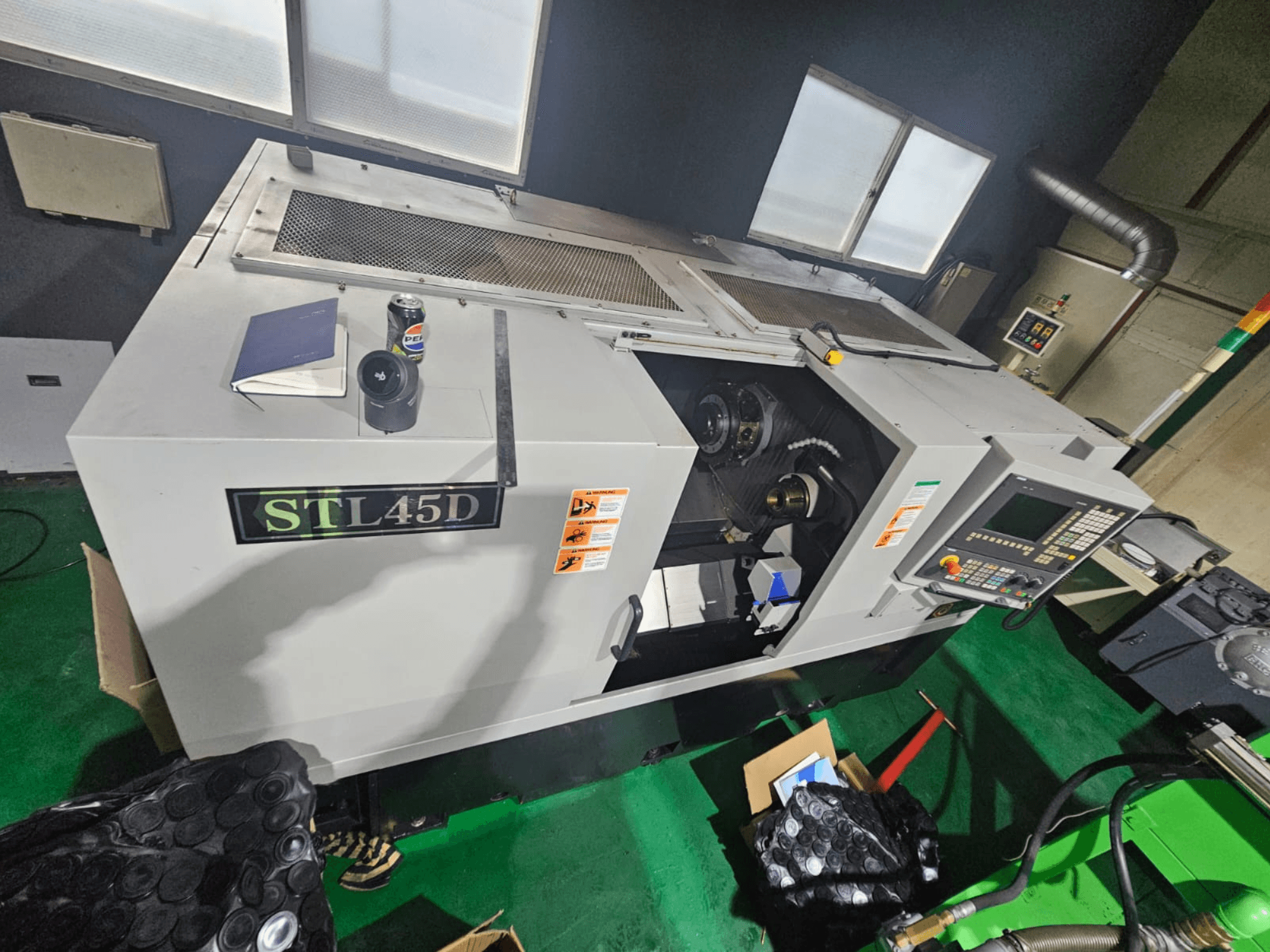 STL45D CNC-kone ylhäältä katsottuna, jossa näkyy ohjauspaneeli, lieriömäinen osa, kannettava tietokone ja tölkki päällä.