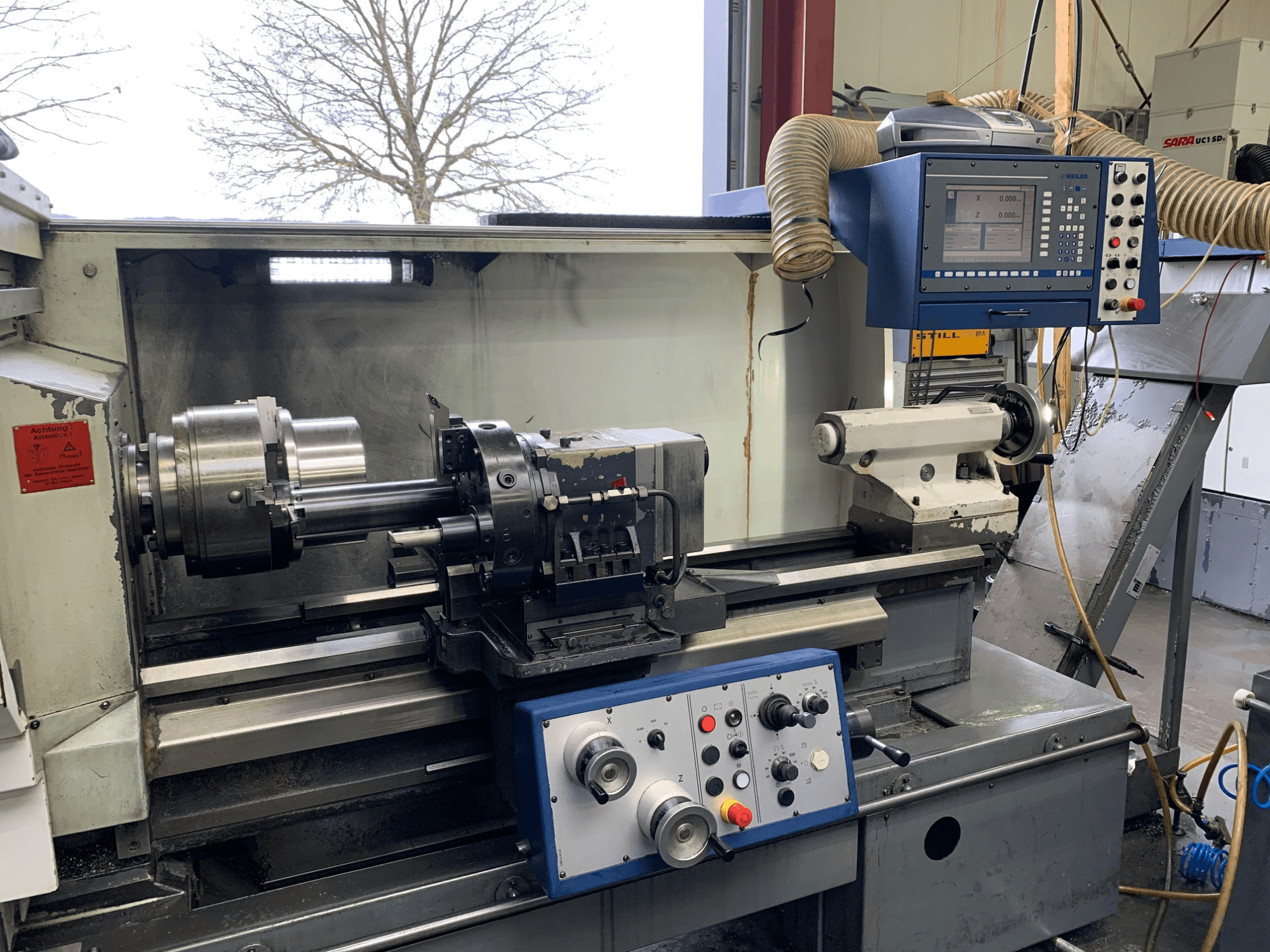 Weiler E55X1000 -vaakasorvauskone työpajassa, jossa näkyy ohjauspaneeli, sorvi ja työkalunpidin. Etukuva.