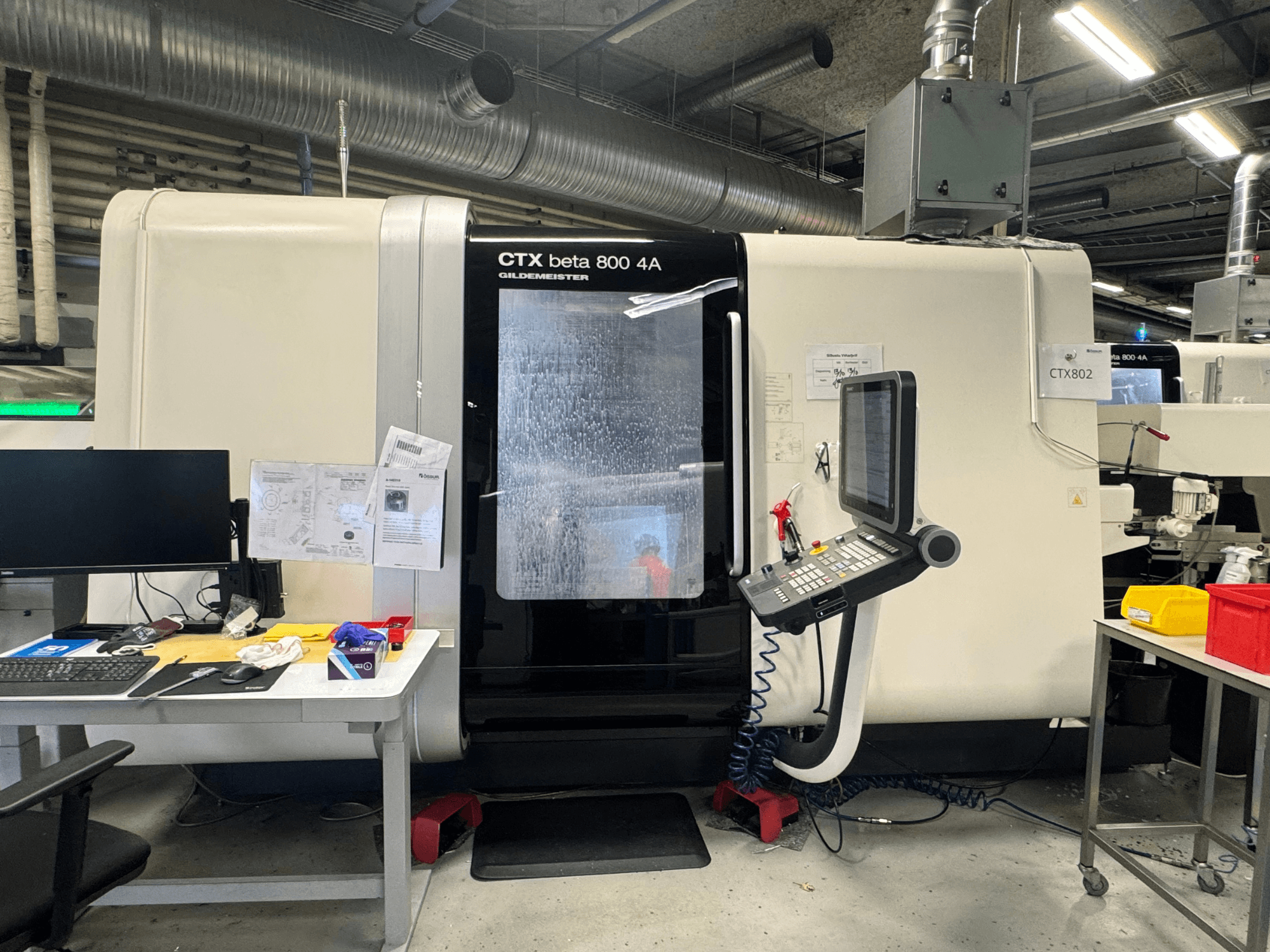 CTX beta 800 4A CNC-kone työpajassa, sivukuva, jossa näkyy ohjauspaneeli ja työtila täynnä työkaluja ja asiakirjoja.