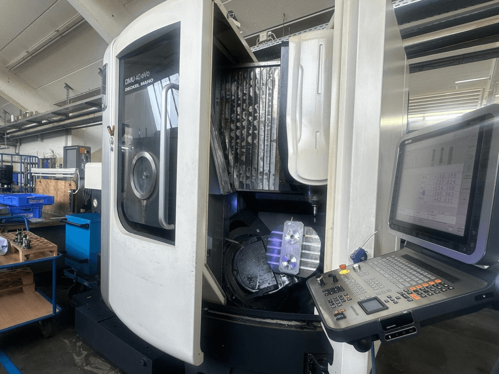 Deckel Mahon DMU 40 eVo -jyrsinkone työpajassa, etukuva, jossa näkyy ohjauspaneeli ja metallikappale karassa.