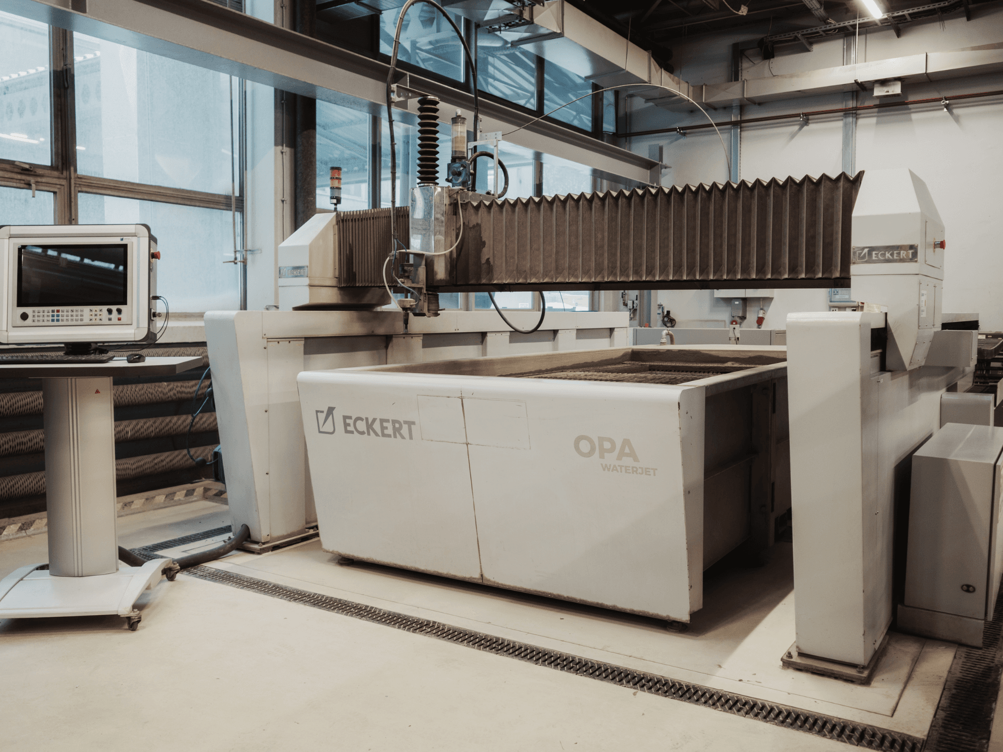 ECKERT OPAL -vesileikkauskone työpajassa, kuvattu edestäpäin, ohjauspaneeli vieressä.