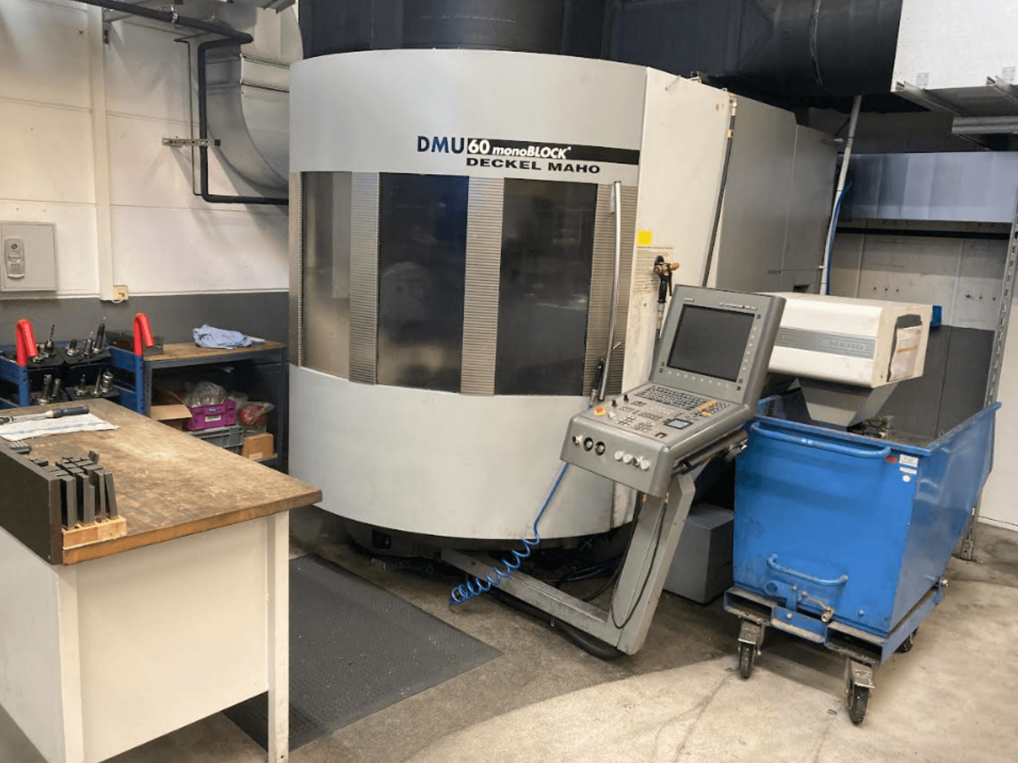 DMG MORI DMU 60 Monoblock -pystytyöstökeskus, etukuva, jossa ohjauspaneeli, työtila ja sininen työkalukärry näkyvissä.