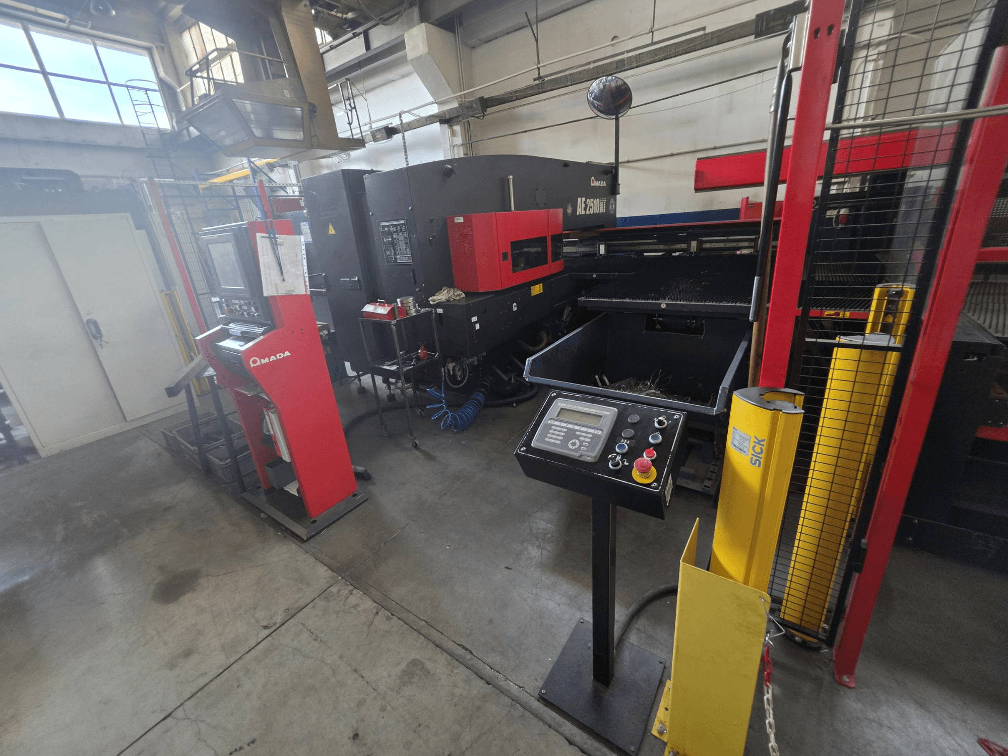 CNC-lävistyskone AMADA AE-2510NT, etunäkymä ohjauspaneelista, turvallisuusominaisuuksista ja ympäröivästä teollisuusympäristöstä.