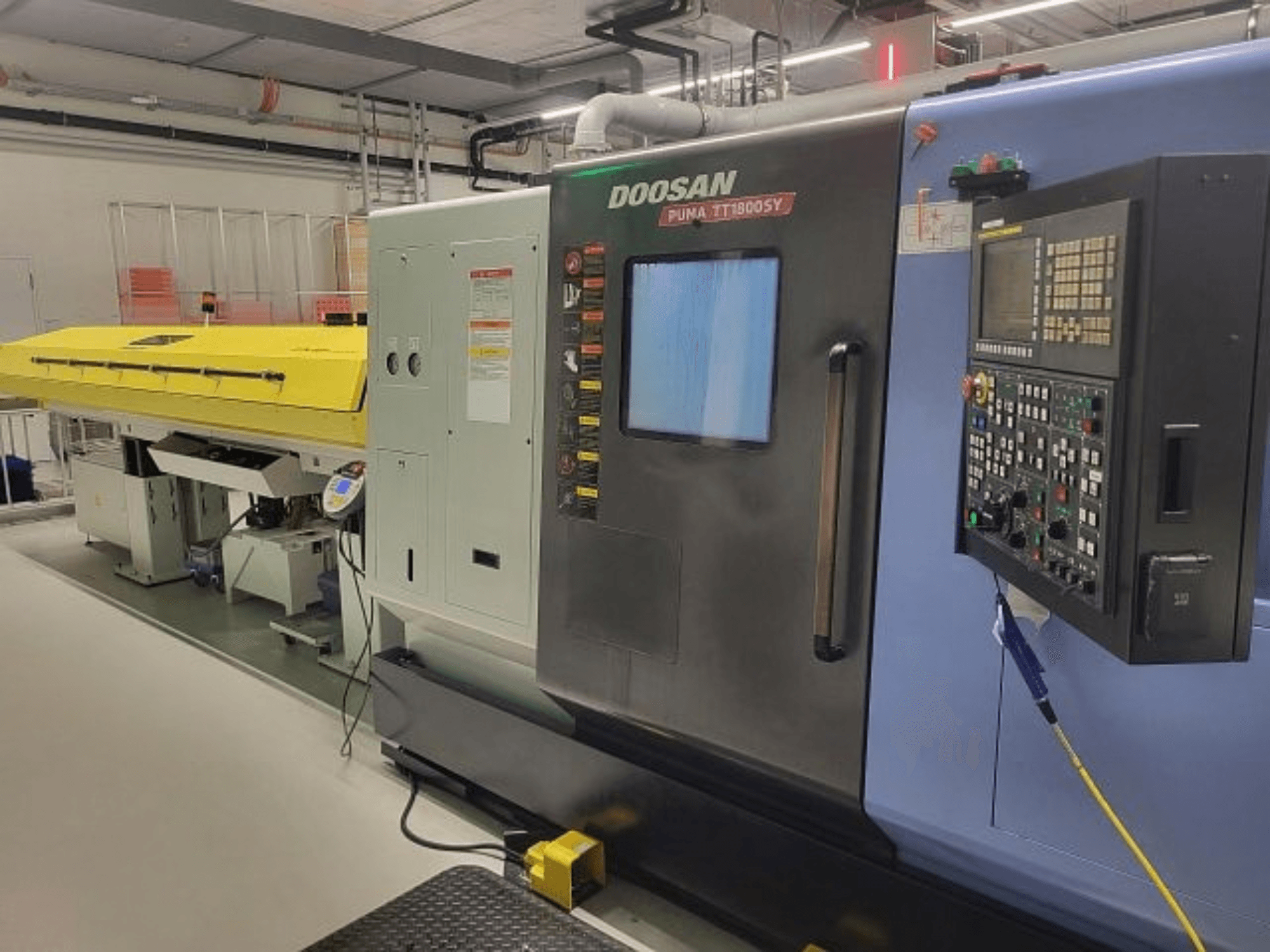 DOOSAN PUMA TT 1800 SY -koneistuskeskus, etunäkymä ohjauspaneelilla ja keltaisella suojuksella, teollisuusympäristössä.