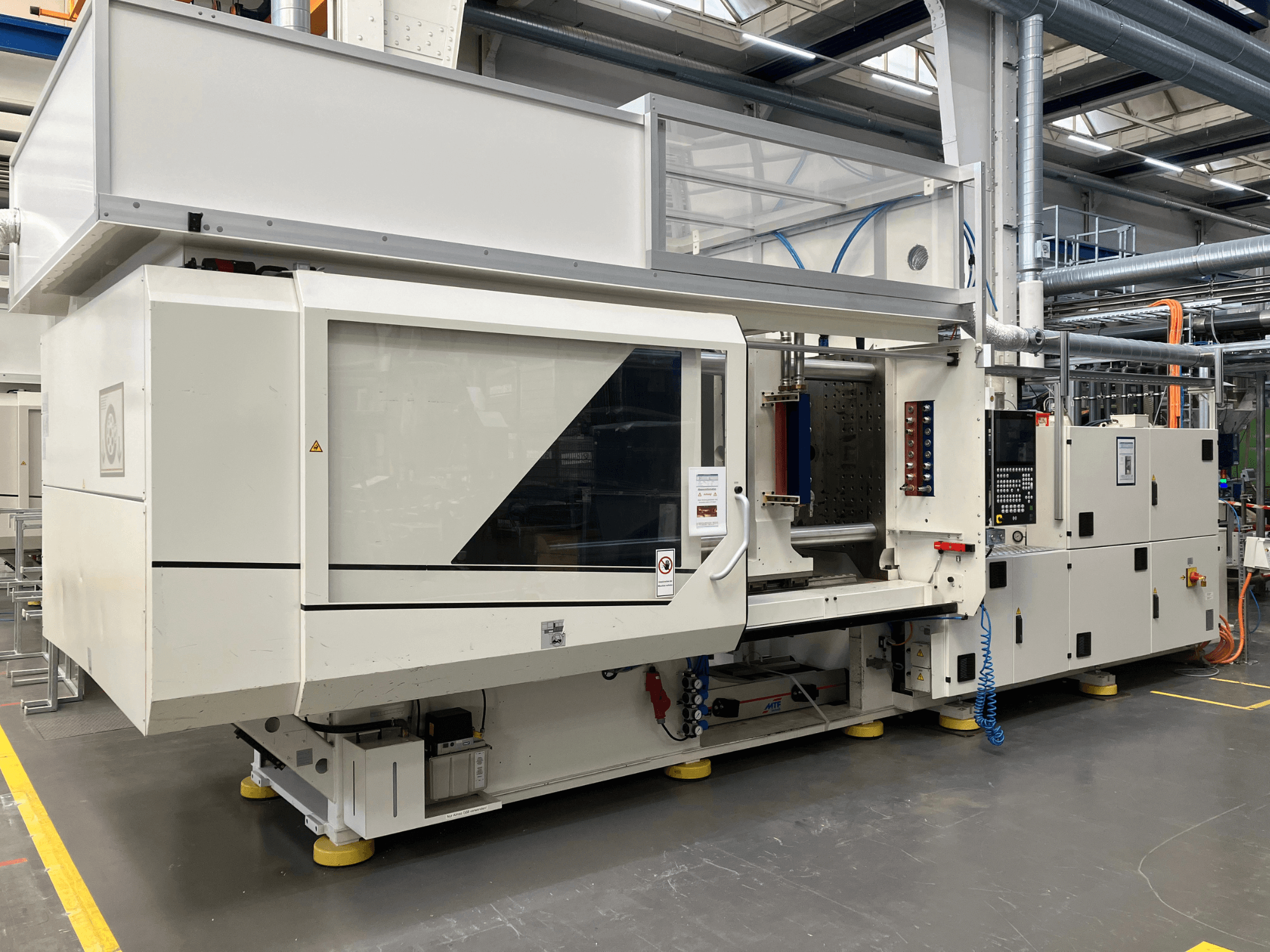 Sivukuva AET-mallin ruiskuvalukoneesta, jossa on ohjauspaneeli ja läpinäkyvät kannet, teollisuusympäristössä.