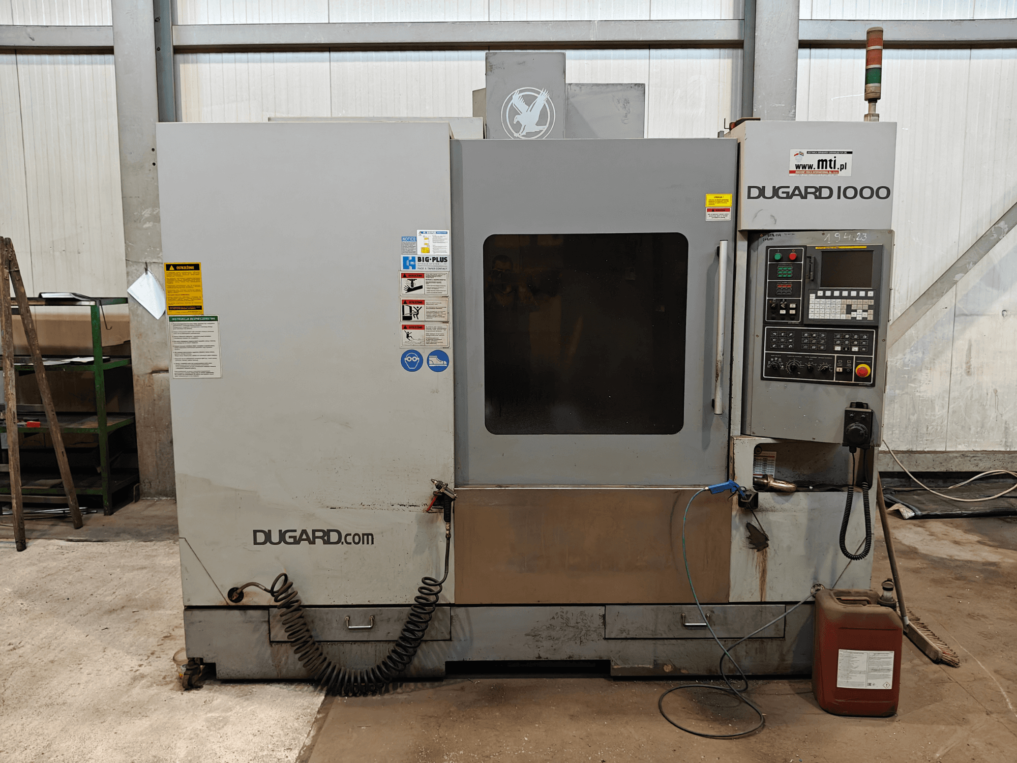 Dugard 1000 CNC -kone, etukuva, jossa näkyy ohjauspaneeli, turvatarrat ja öljysäiliö, työpajassa.