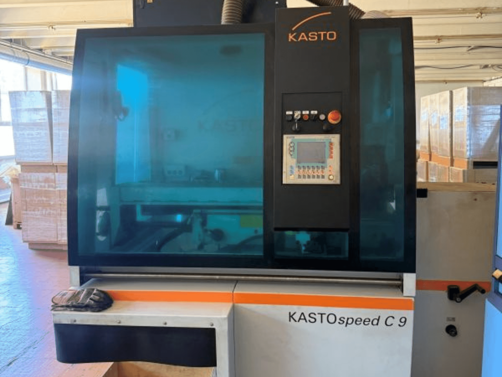 KASTO KASTOspeed C 9 -pyörösahan etunäkymä, jossa näkyy ohjauspaneeli ja turvalasi; taustalla puulaatikoita.