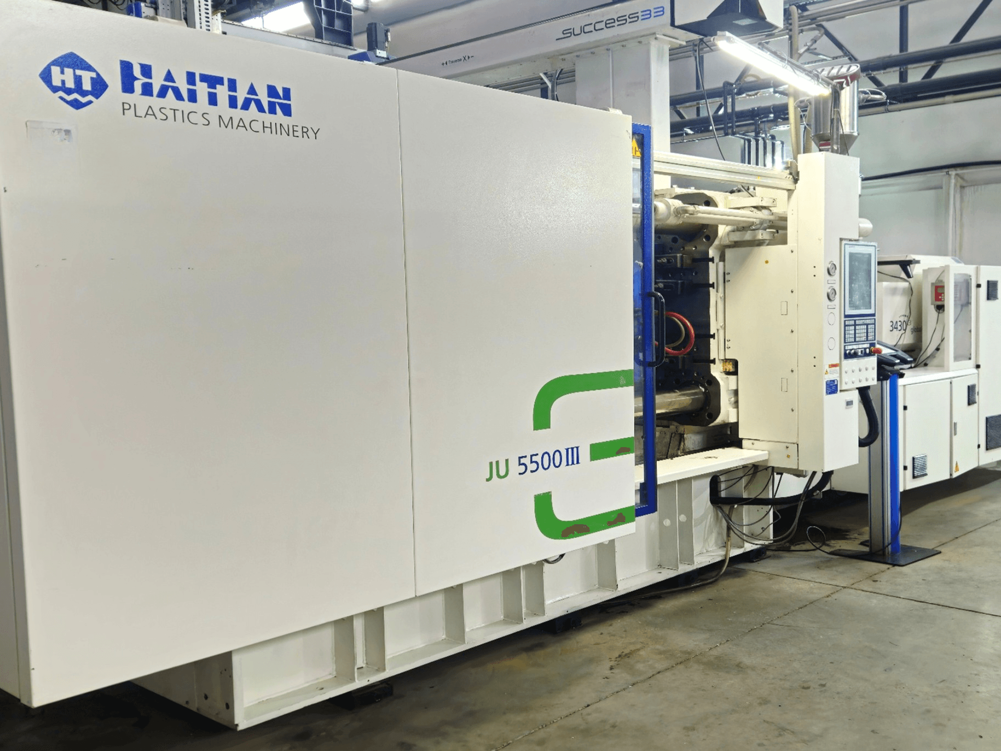 Haitin JU 5500III -muovikone tehtaalla, etukuva ohjauspaneelista ja tuotantoalueesta.