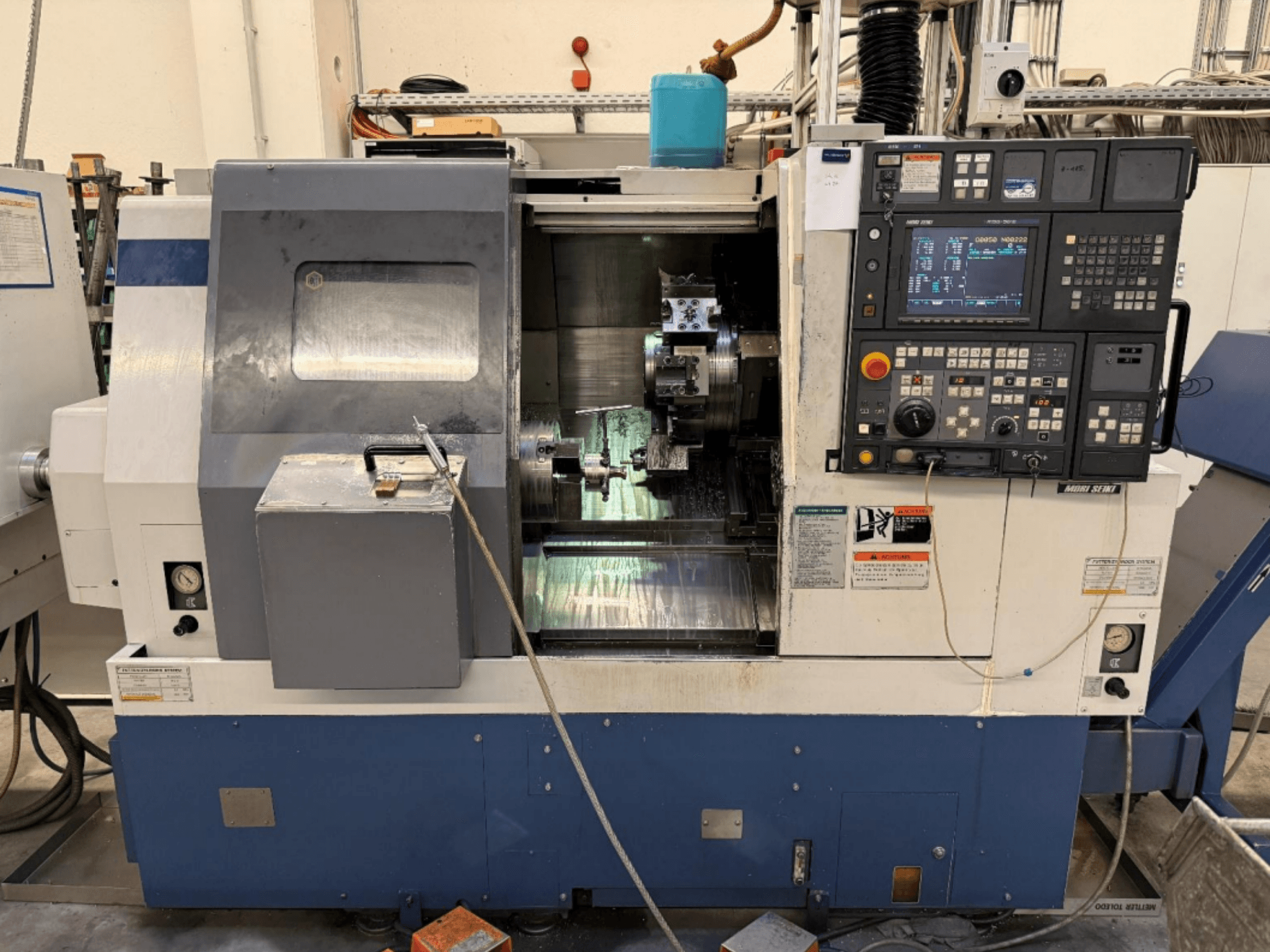 MORI SEIKI SL-250ASMC -sorvaus-jyrsinkeskus, etunäkymä, jossa näkyy ohjauspaneeli ja työkappaleen kiinnitin toiminnassa.